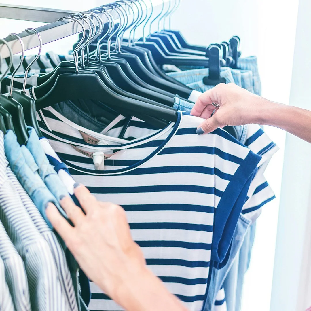 Person browsing striped shirts on clothing rack