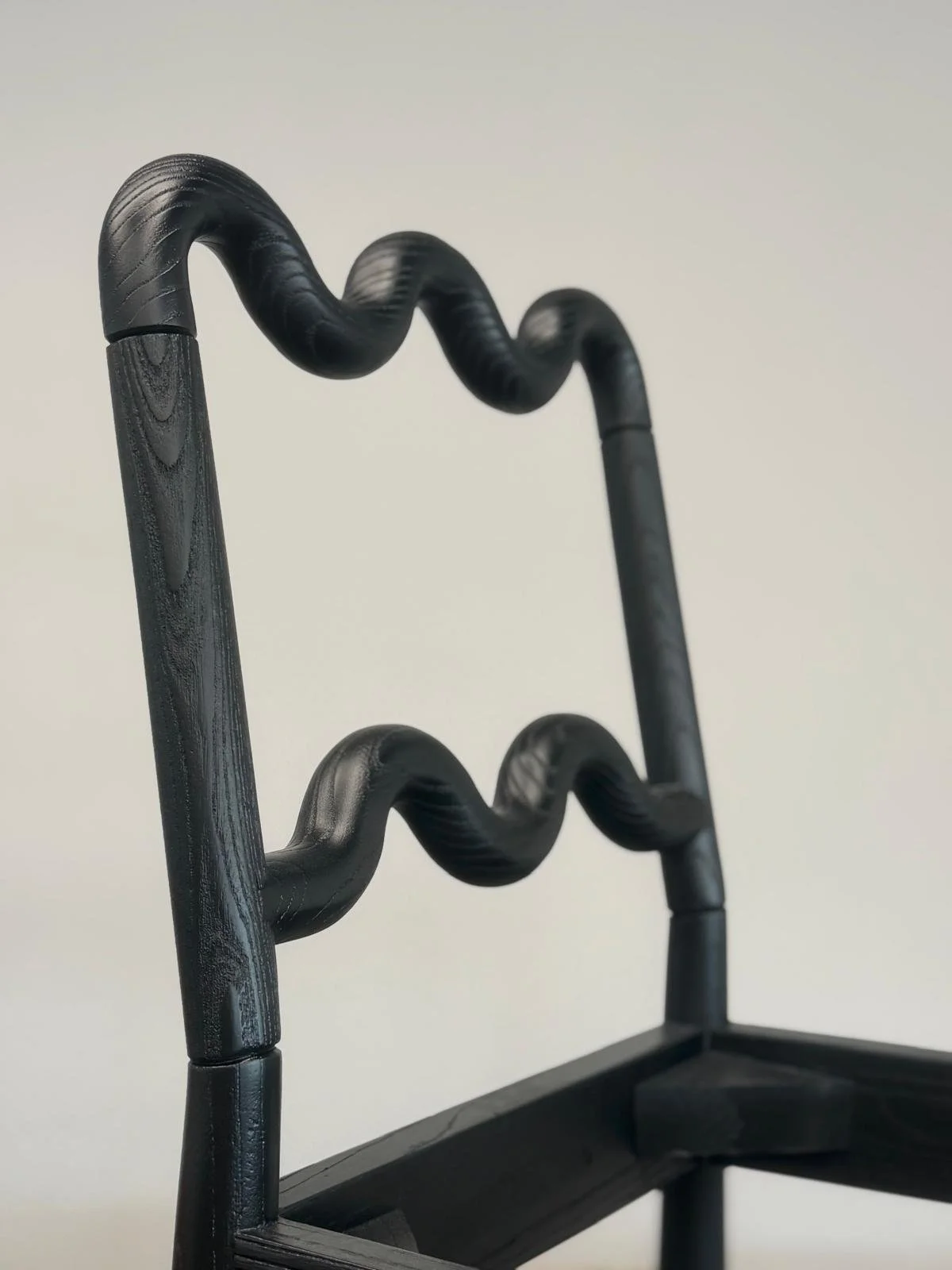Close-up of a black walnut dining chair with a wave pattern on the sides against a plain white background.