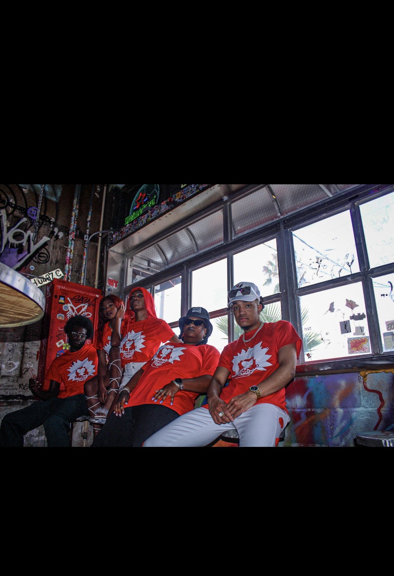 Group of people wearing matching red and white shirts inside a graffiti-covered room with windows.