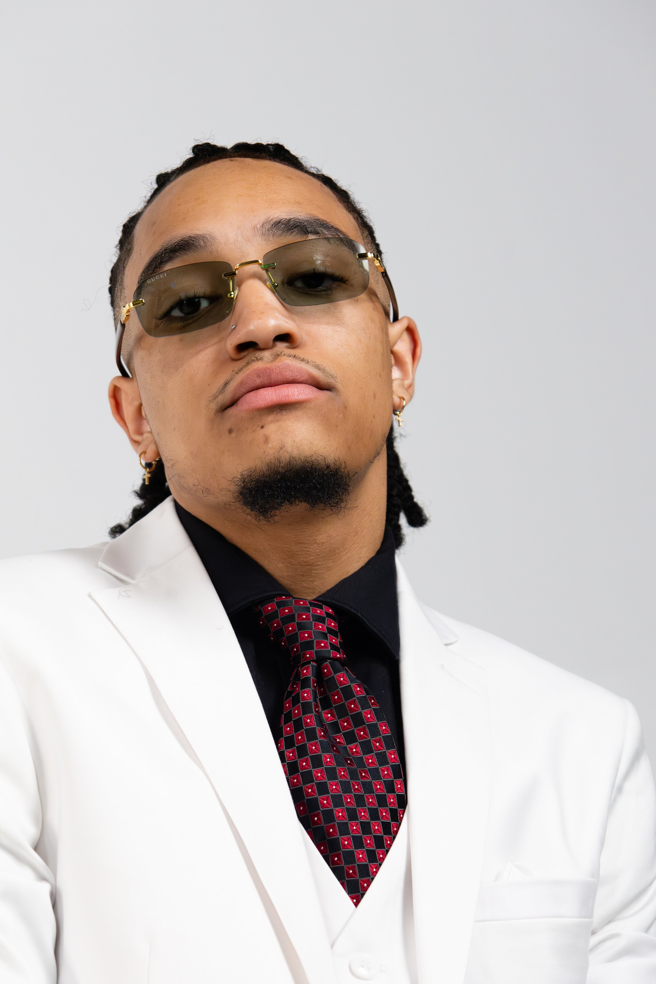Man in white suit and sunglasses with a red and black tie.