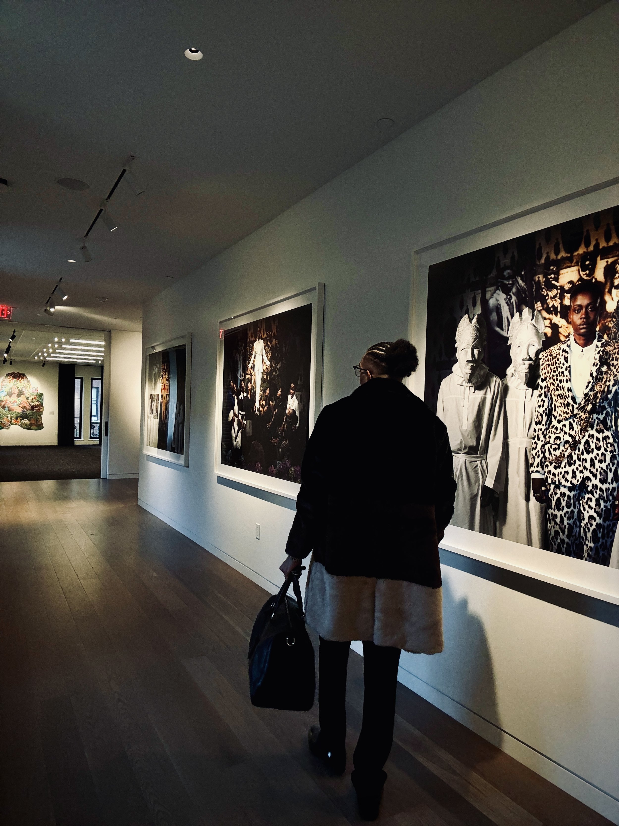 Person walking through an art gallery with framed artworks on the wall.