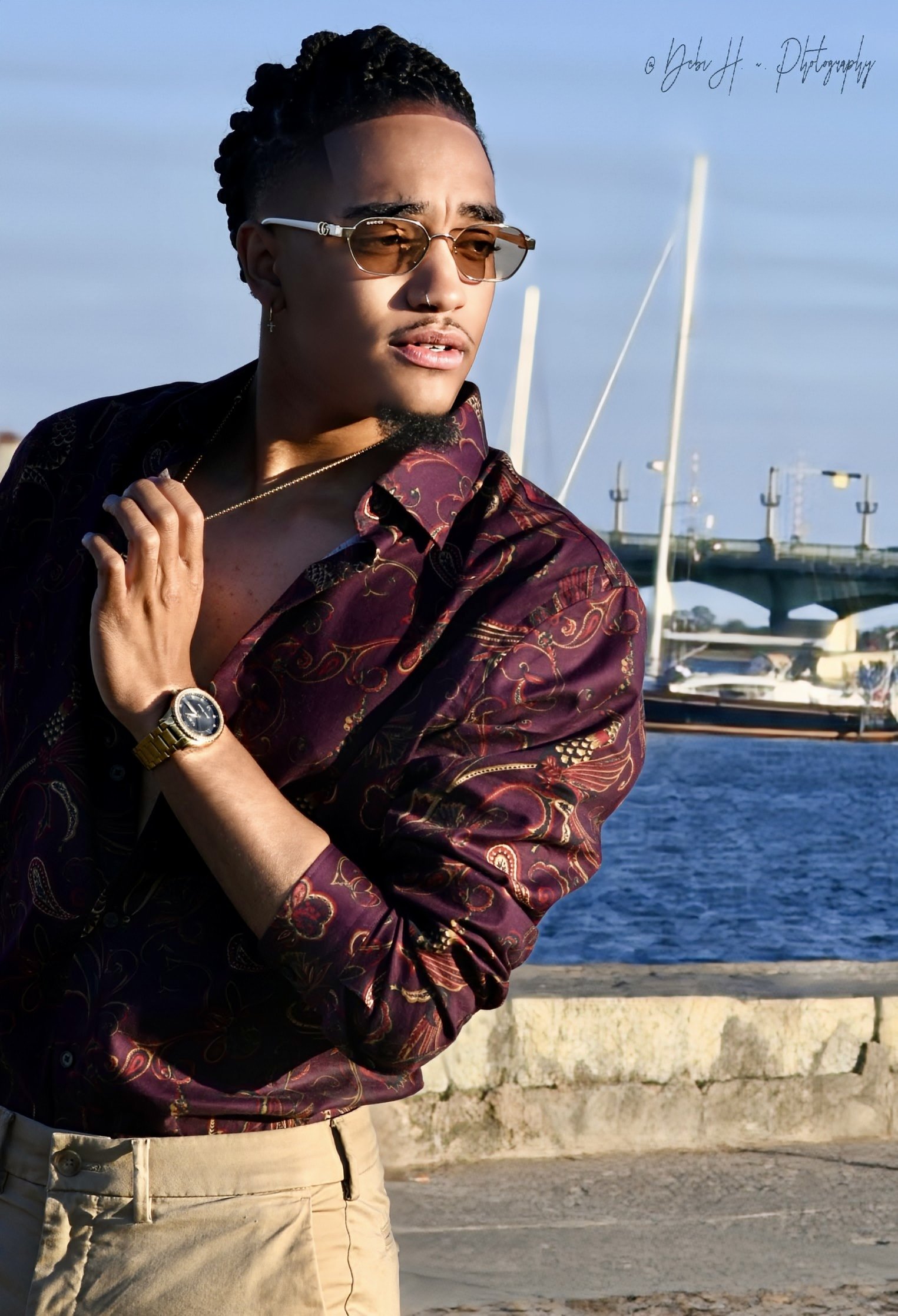 Man with sunglasses wearing a patterned shirt by the waterfront.