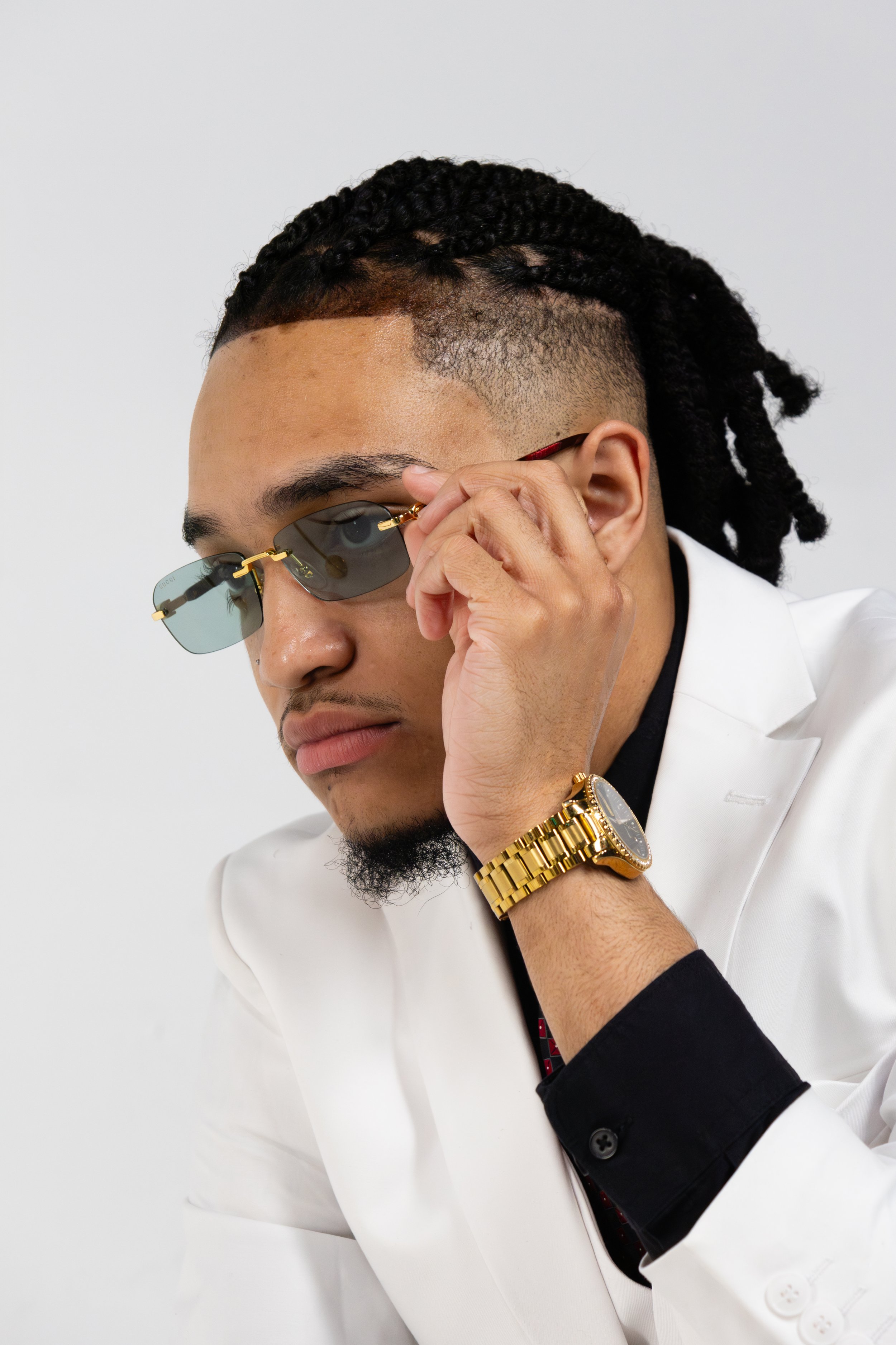 Man wearing sunglasses, white suit, and gold watch