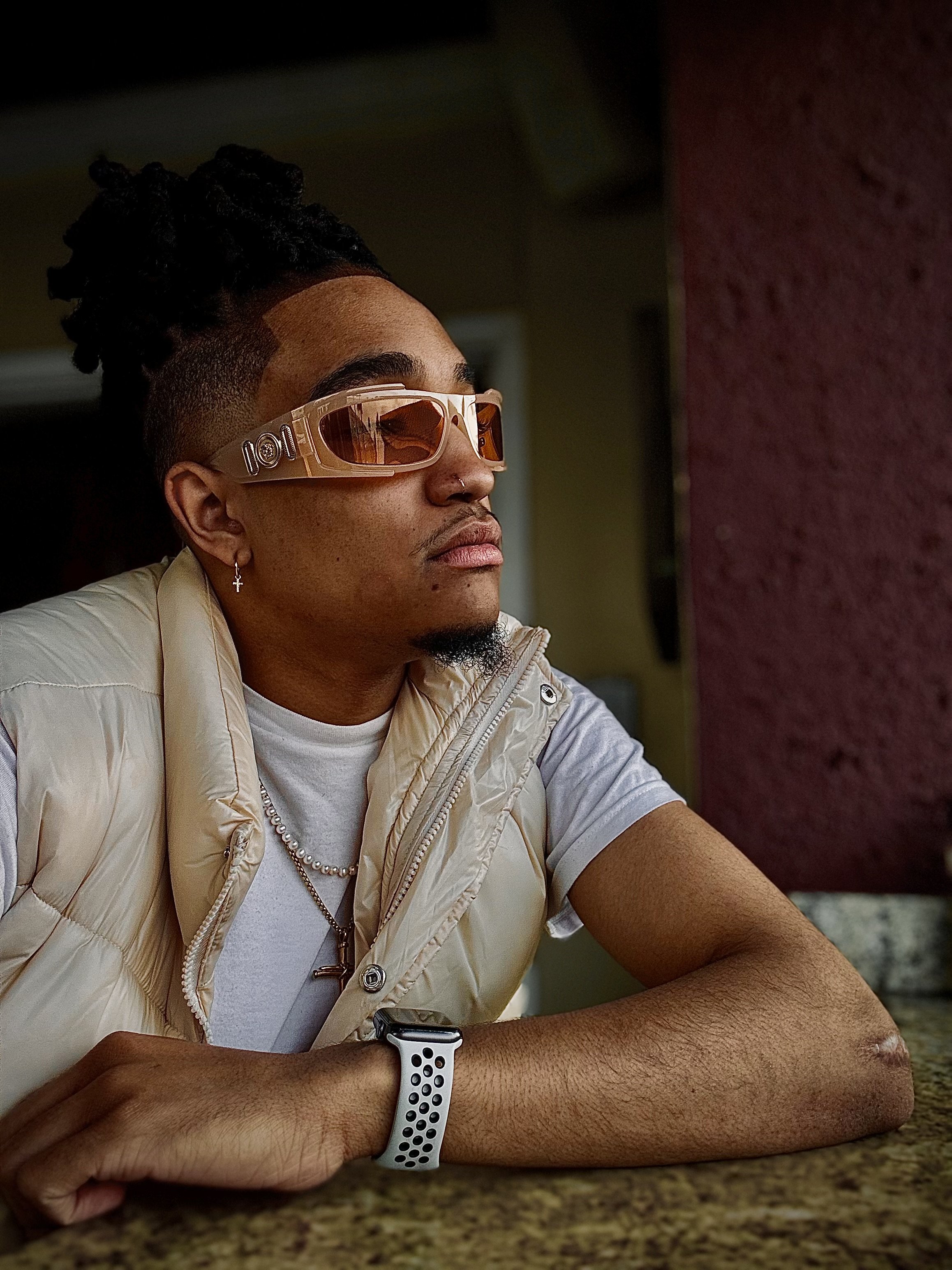 Person wearing large sunglasses, a puffer vest, and a smartwatch, looking to the side.
