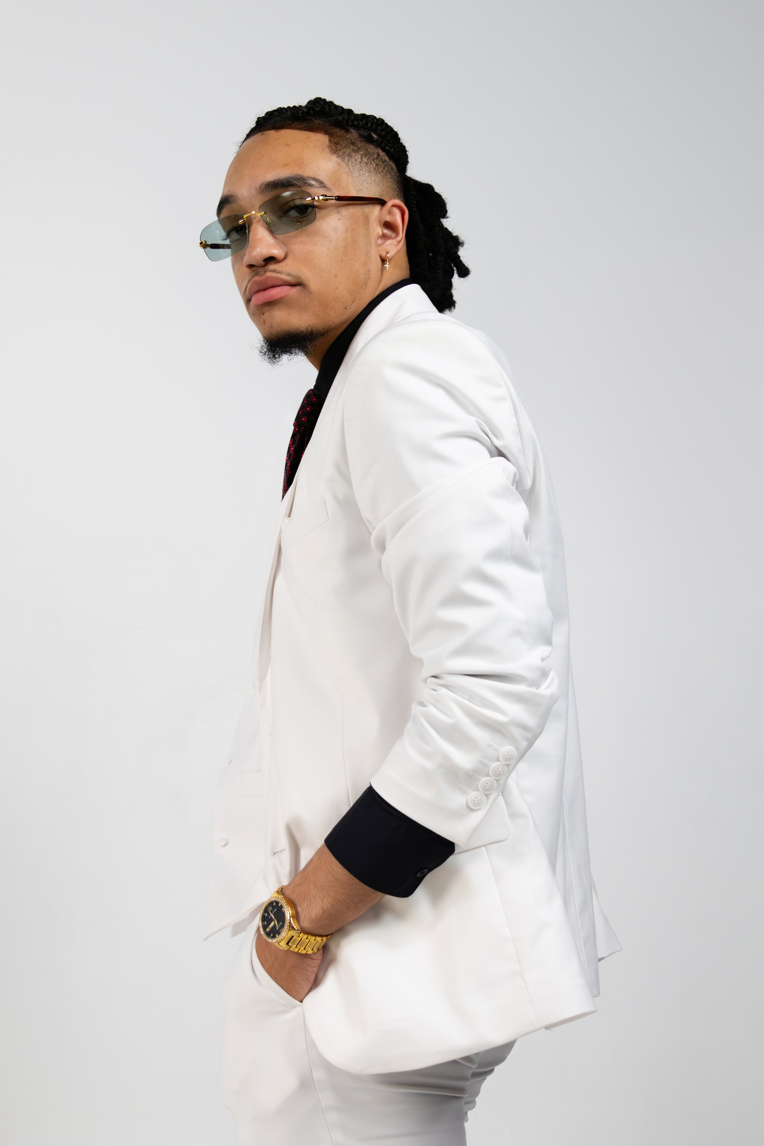 Man in a white suit wearing sunglasses, with a gold watch, looking to the side.