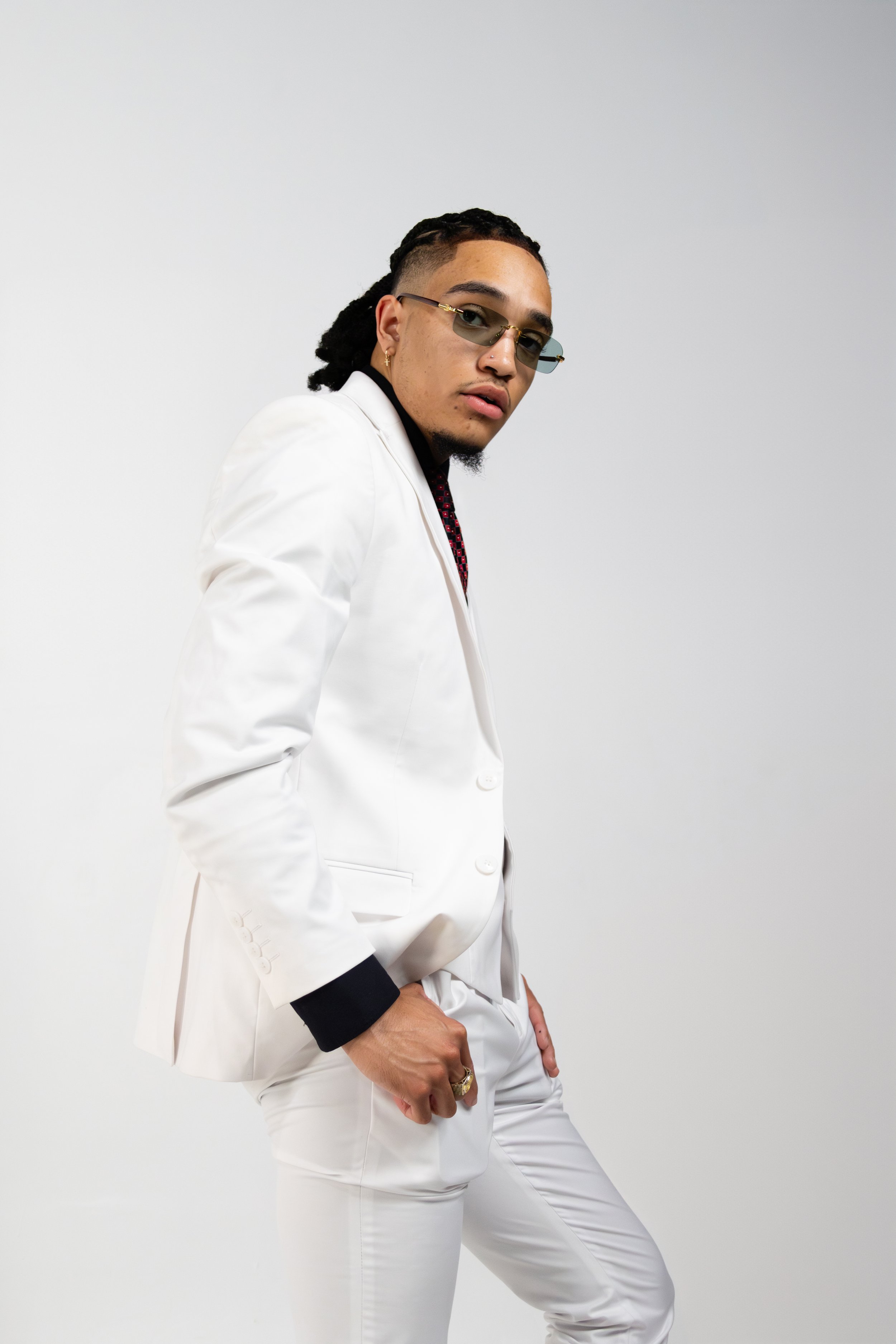 Person wearing a white suit with black accents and sunglasses, posing against a white background.