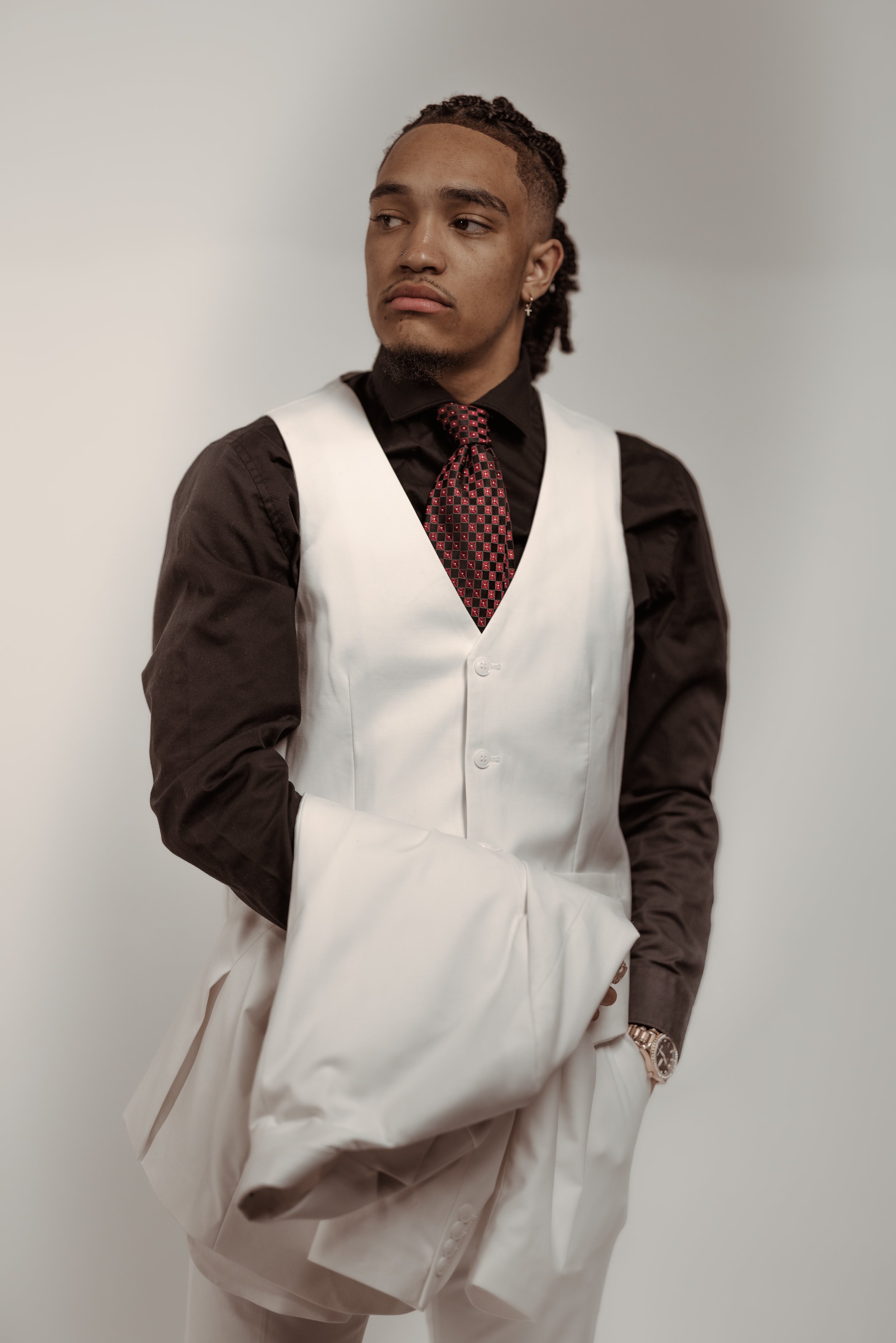 Man in black shirt and white vest with a red tie, holding a white jacket.