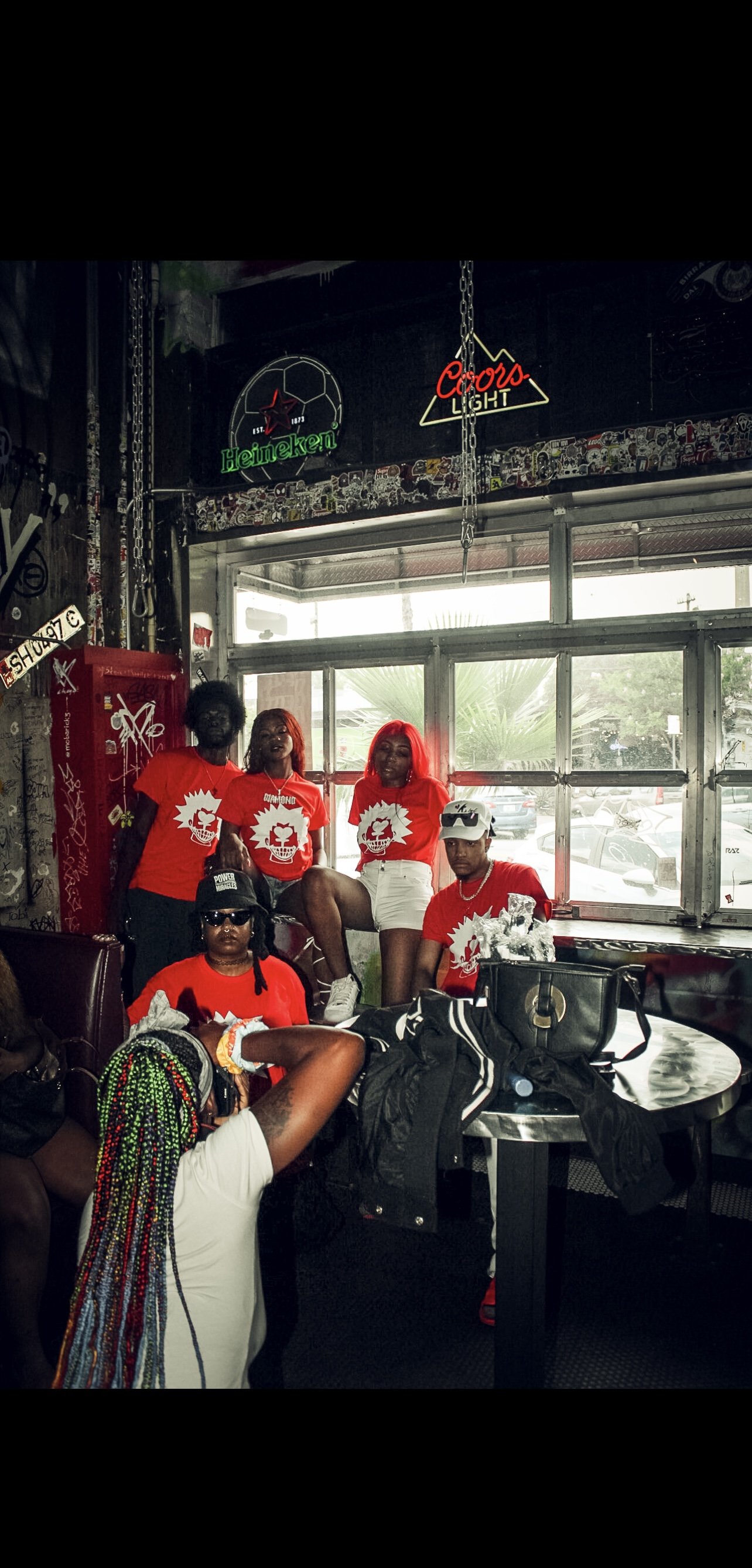 Group of people wearing matching red t-shirts posing in a bar with neon signs and graffiti.