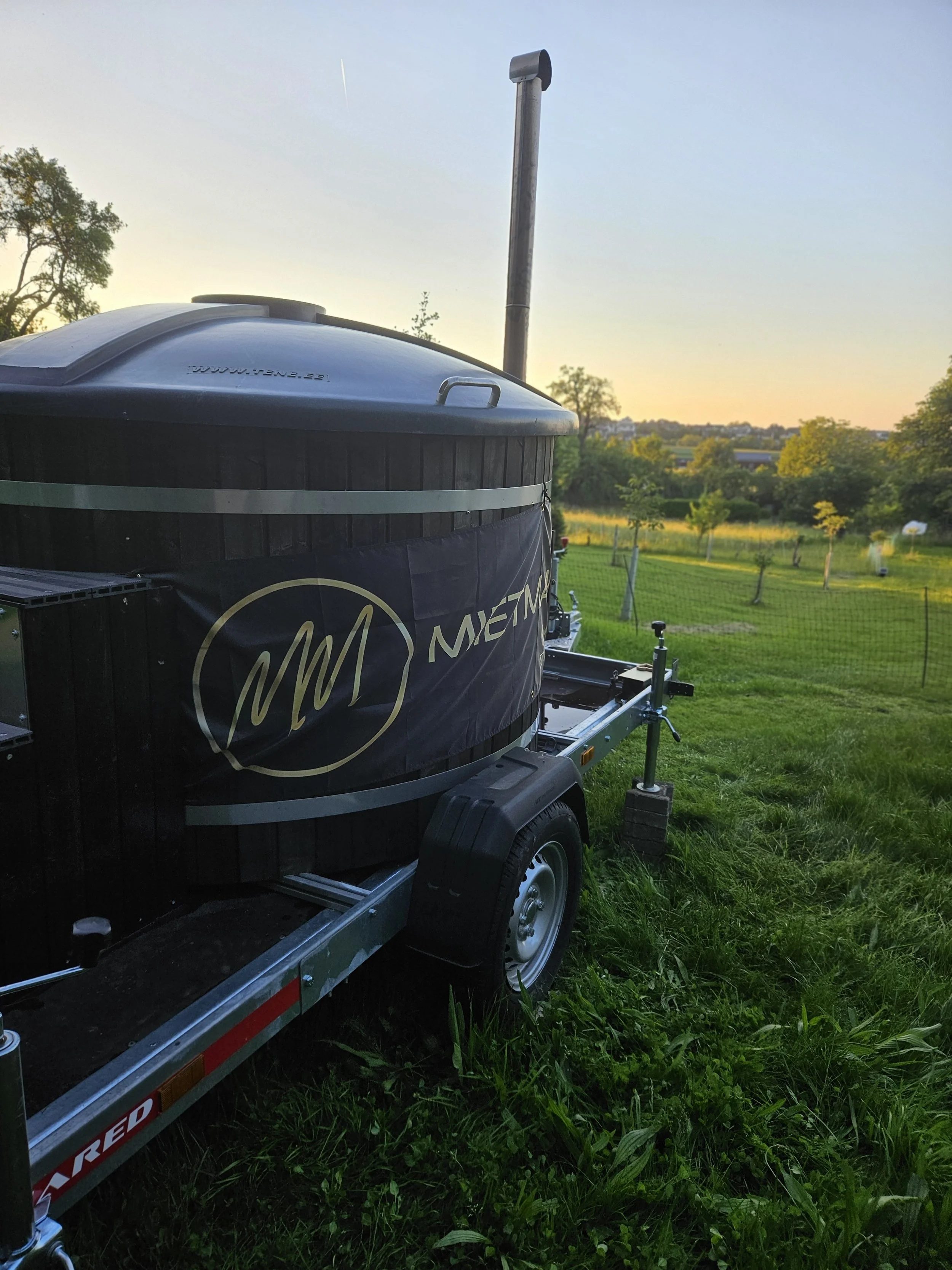 Mobiler HotTub auf einem Anhänger mit Holzofen im freien auf einer Wiese.