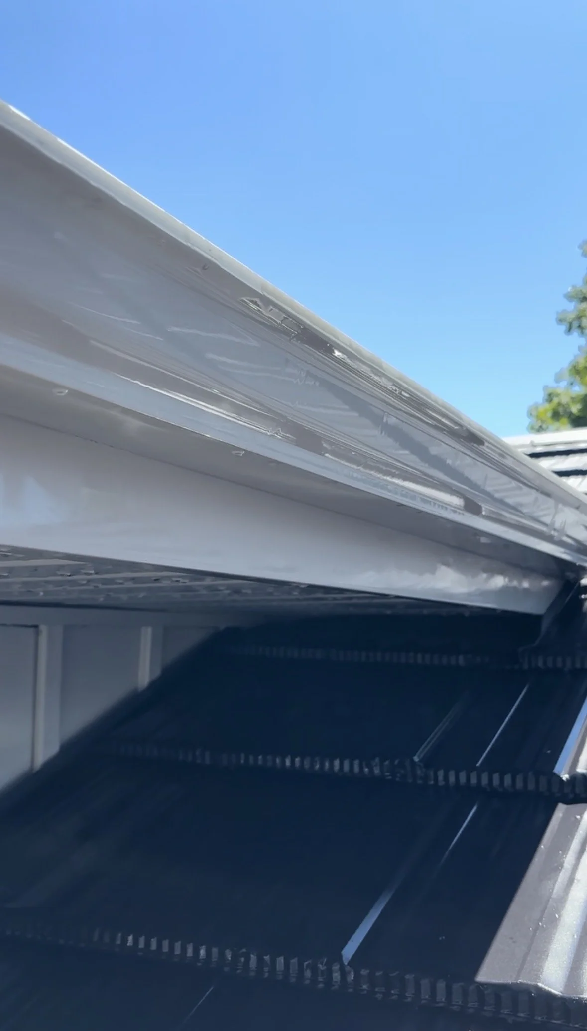 View of an open empty black plastic storage bin outside under a clear blue sky, with part of a silver truck or trailer in the background.