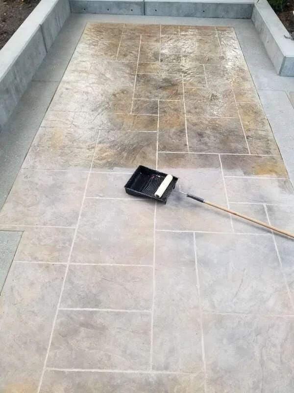 Partially cleaned beige and gray tiled floor with a paint roller tray on a long handle resting on the tiles.
