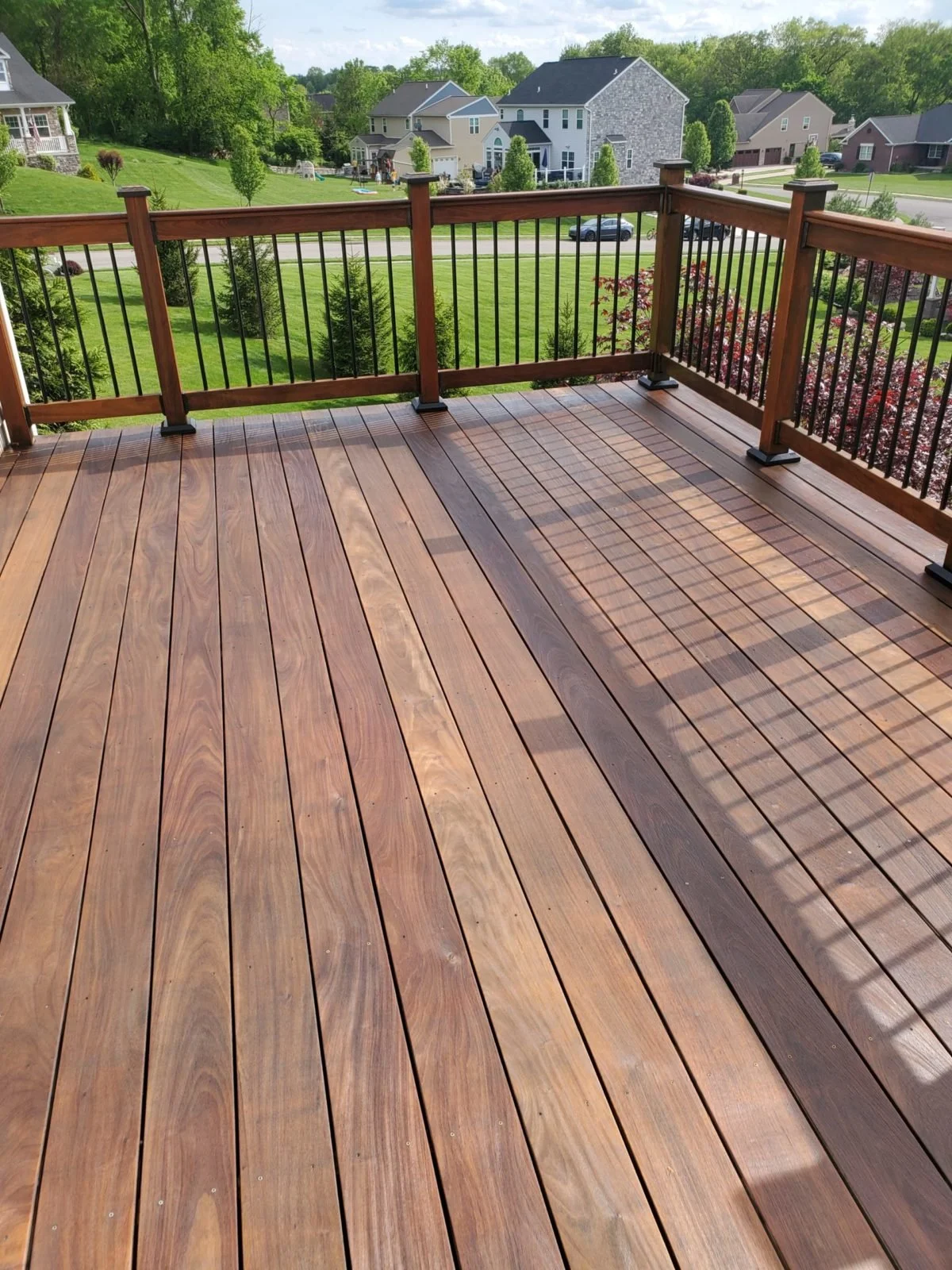 View from a wooden deck with black metal railing overlooking a green, suburban neighborhood with houses and trees.