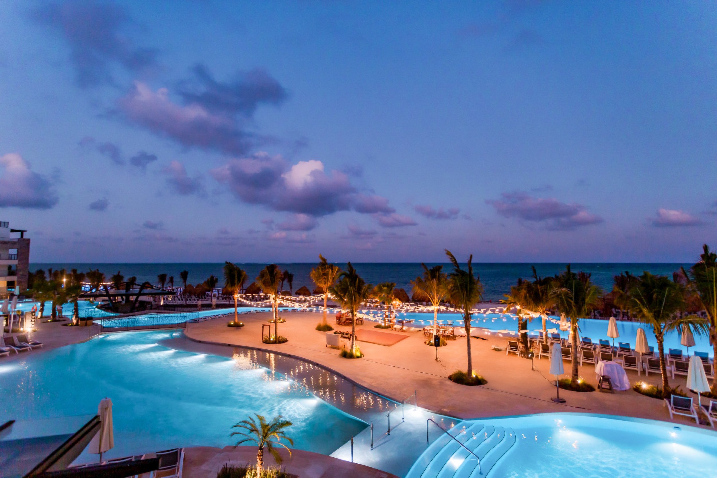 Tropical resort pool area at dusk with palm trees and ocean view