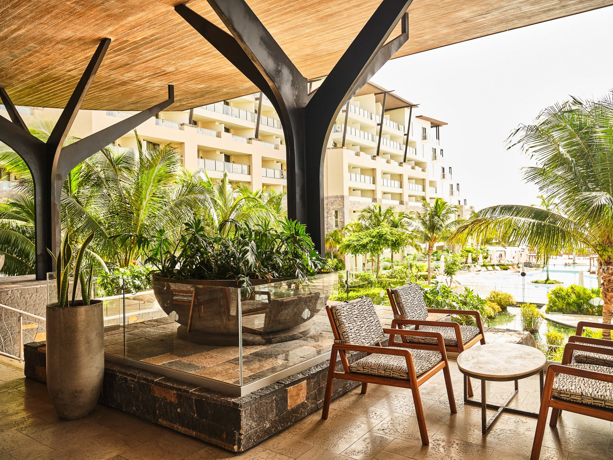Luxurious hotel lobby with outdoor seating, modern architecture, lush tropical garden, and swimming pool view.