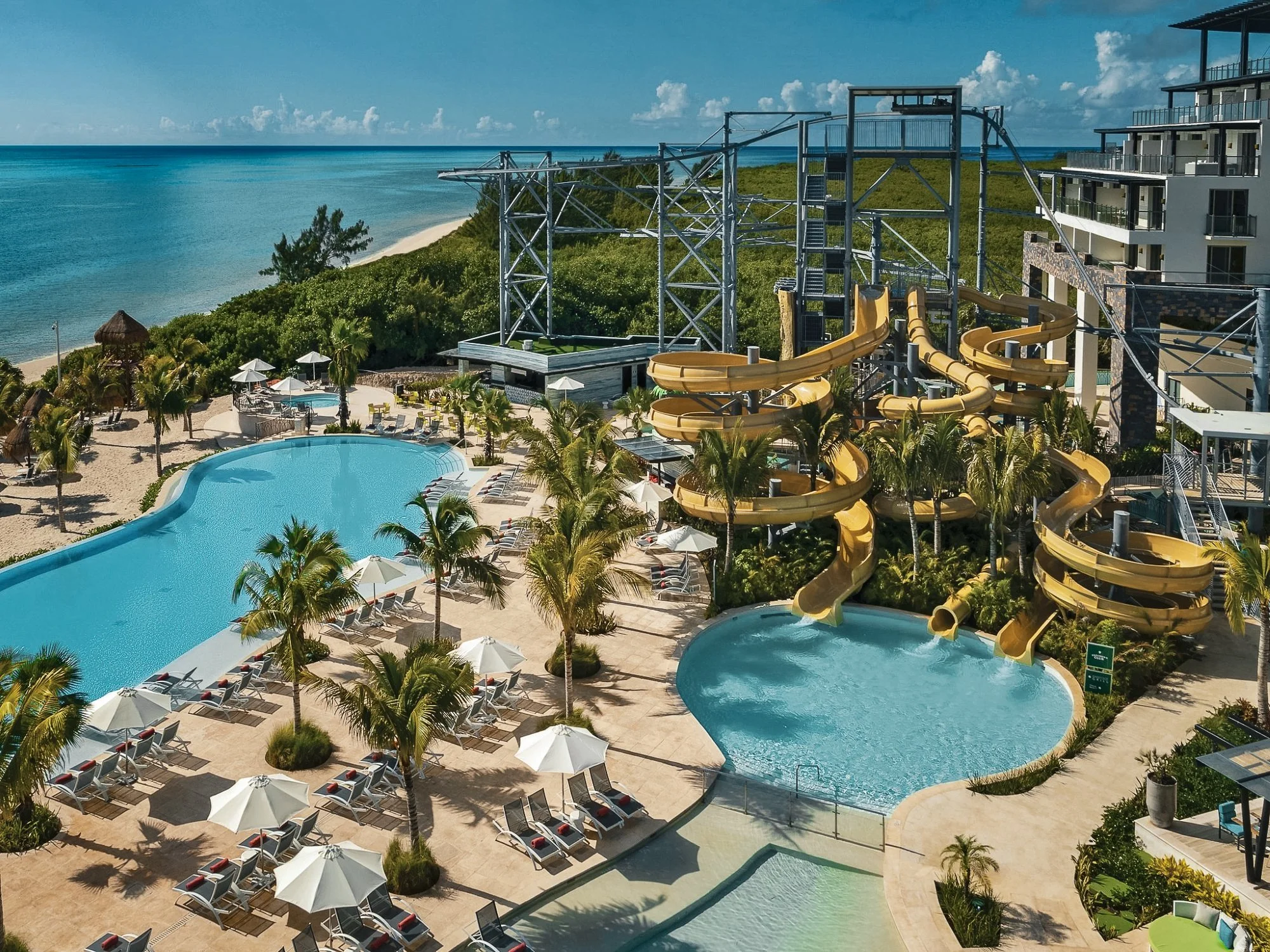 Resort pool area with water slides, palm trees, and ocean view.