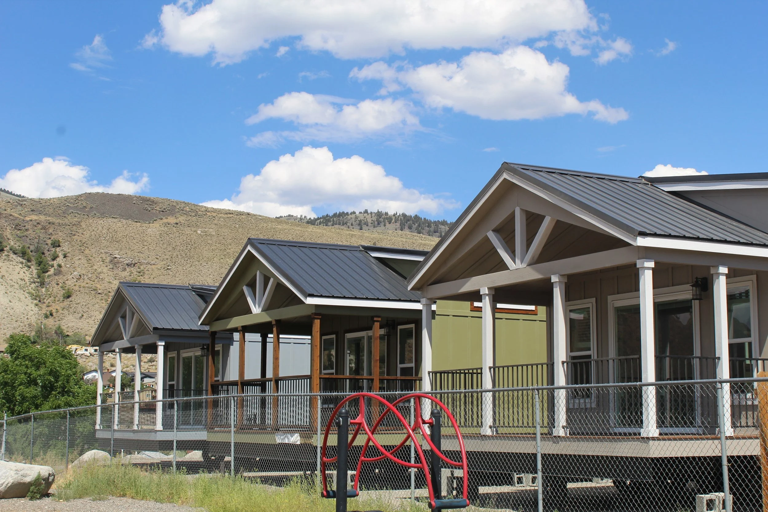 three brand new tiny homes in a row next to a school playground with a mountain in the background