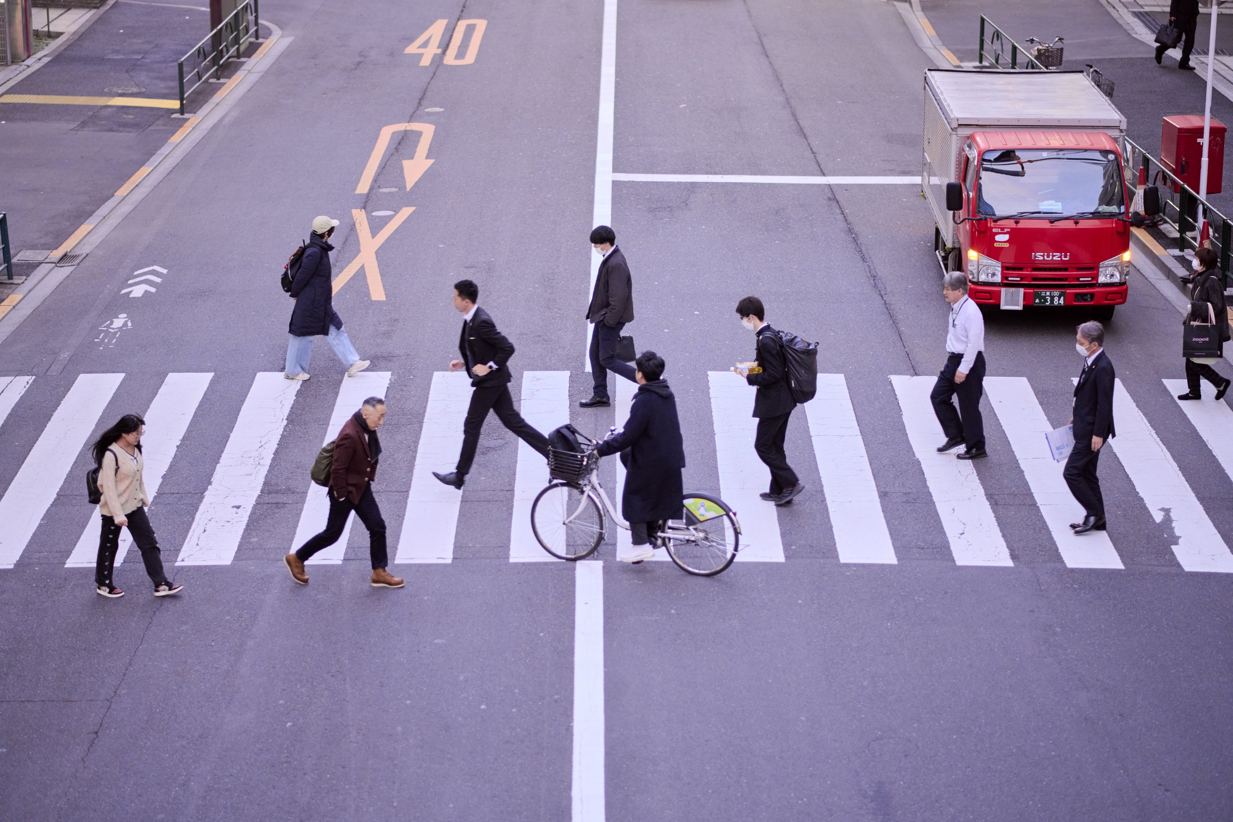 People crossing a city street on a crosswalk, with a red truck parked nearby.