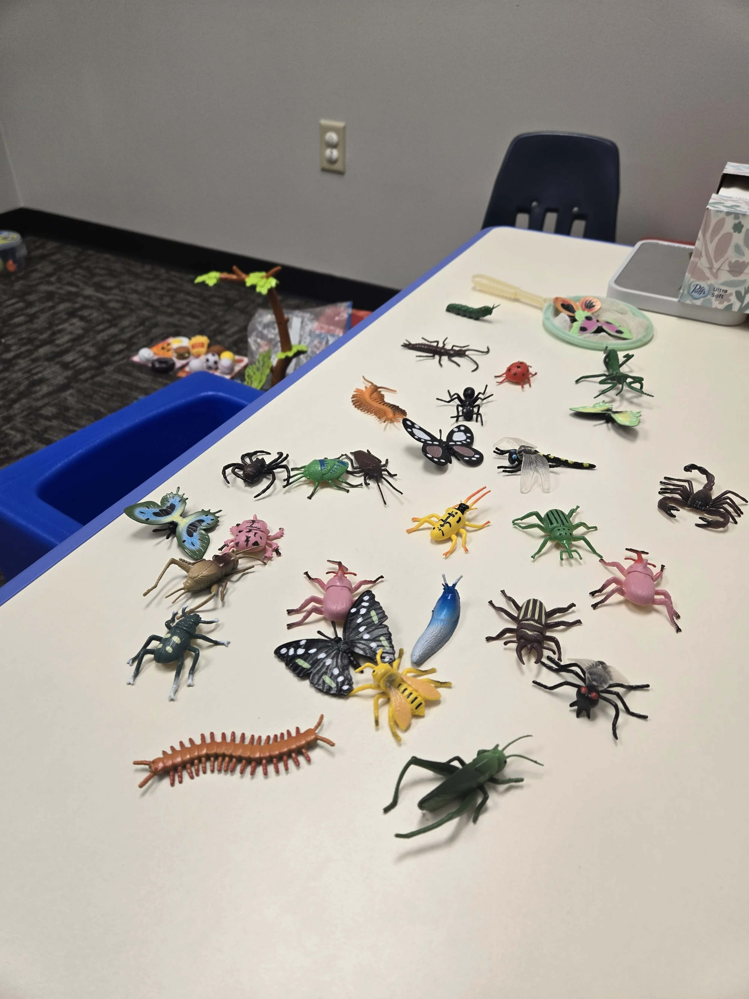 Collection of various colorful toy insects and bugs spread across a white table.