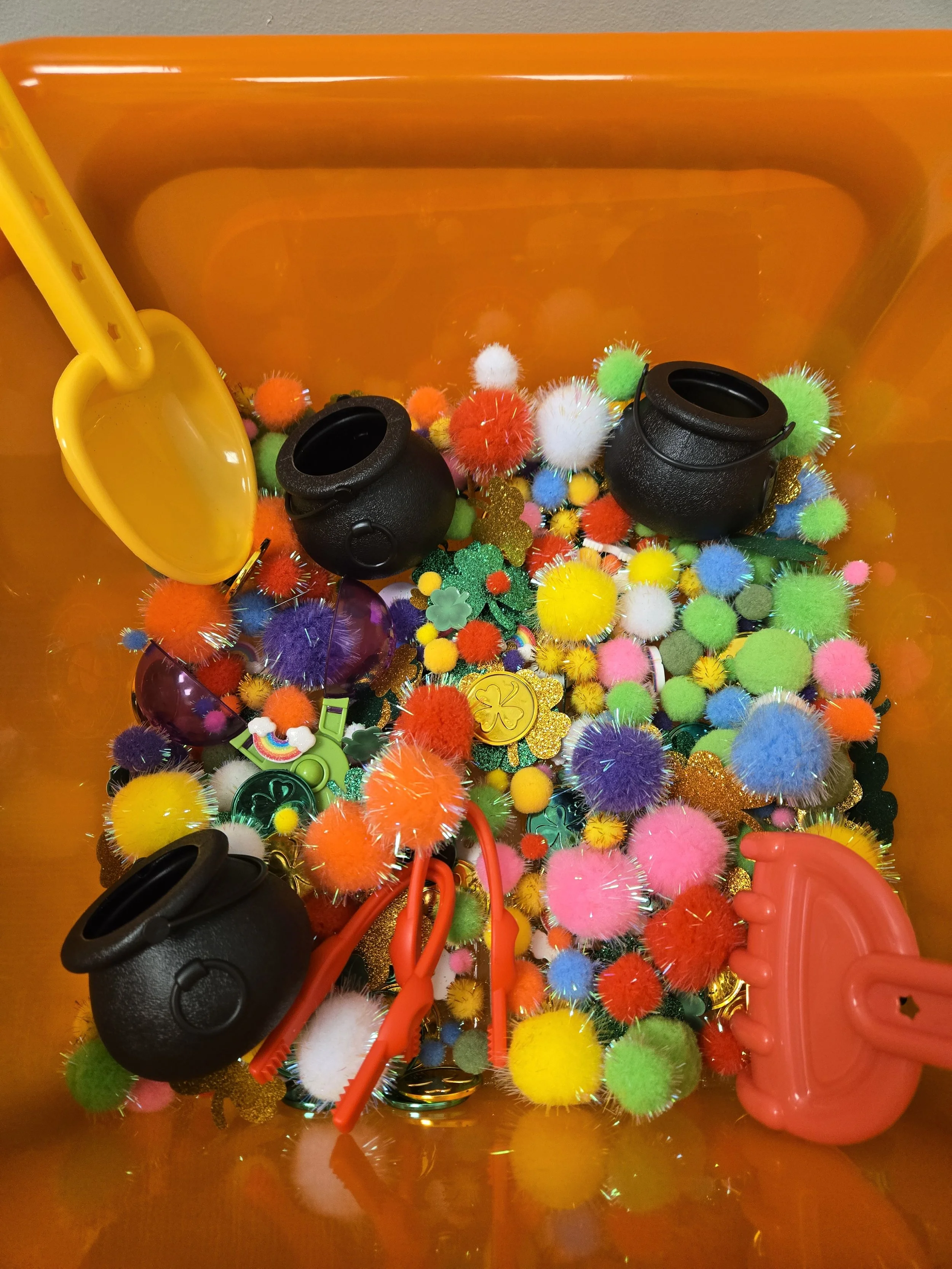 Colorful collection of small fluffy pom-poms, charms, and novelty accessories inside an orange container.
