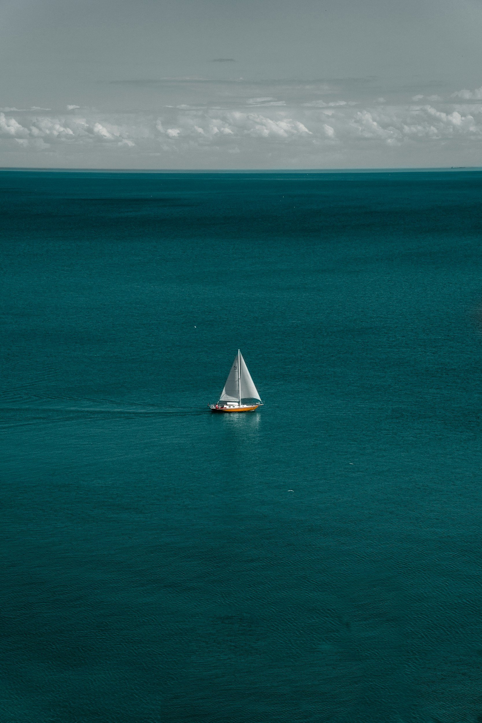 A sailboat sailing on a large body of water with a cloudy sky above.