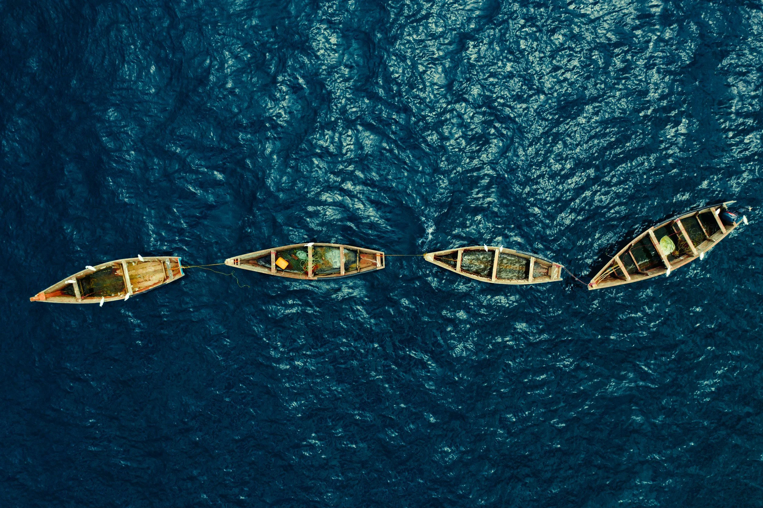 Four wooden boats anchored in the ocean, seen from above, with some personal belongings inside, and surrounded by deep blue water.