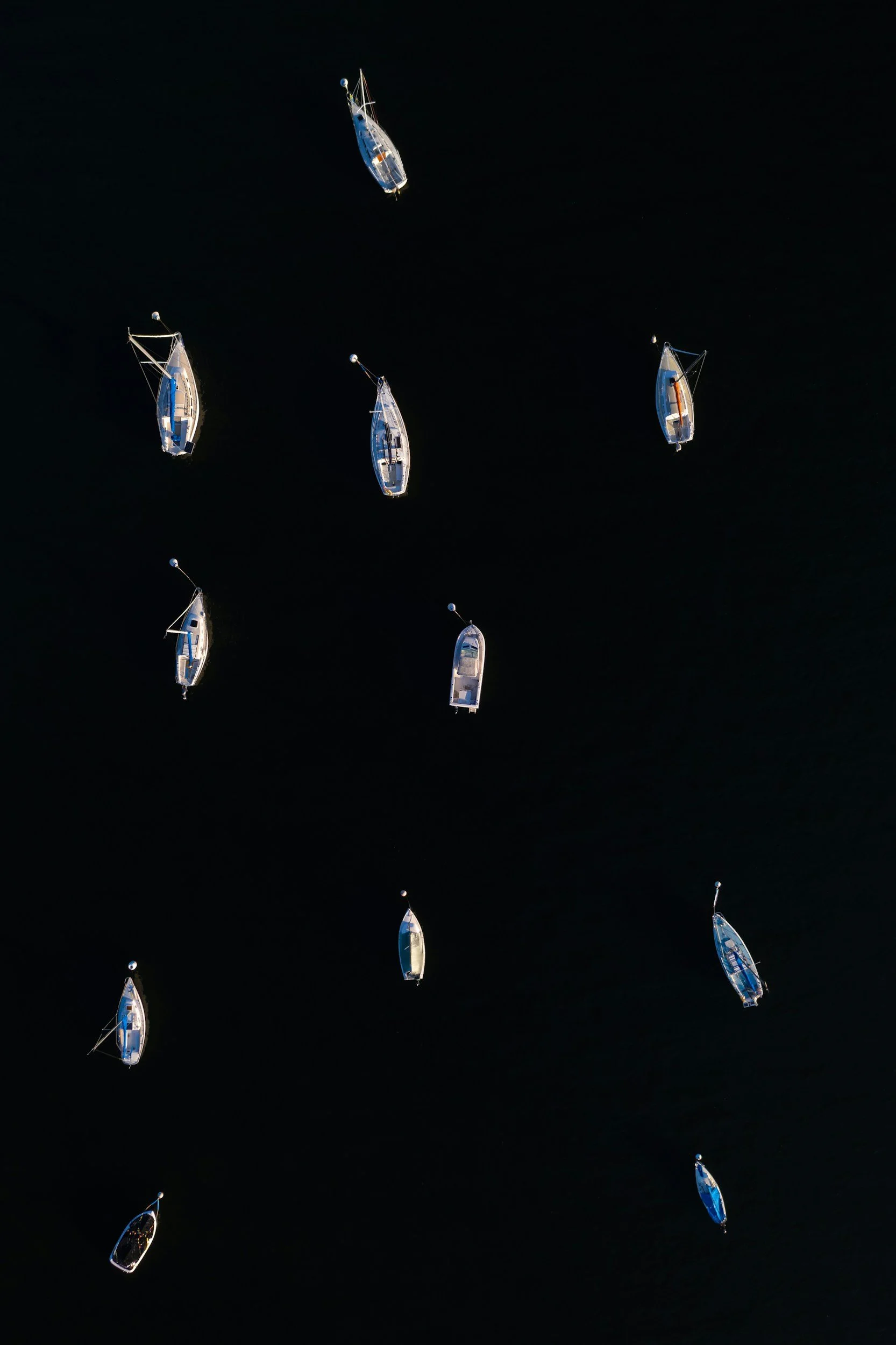 Multiple sailboats floating on dark water, viewed from above.