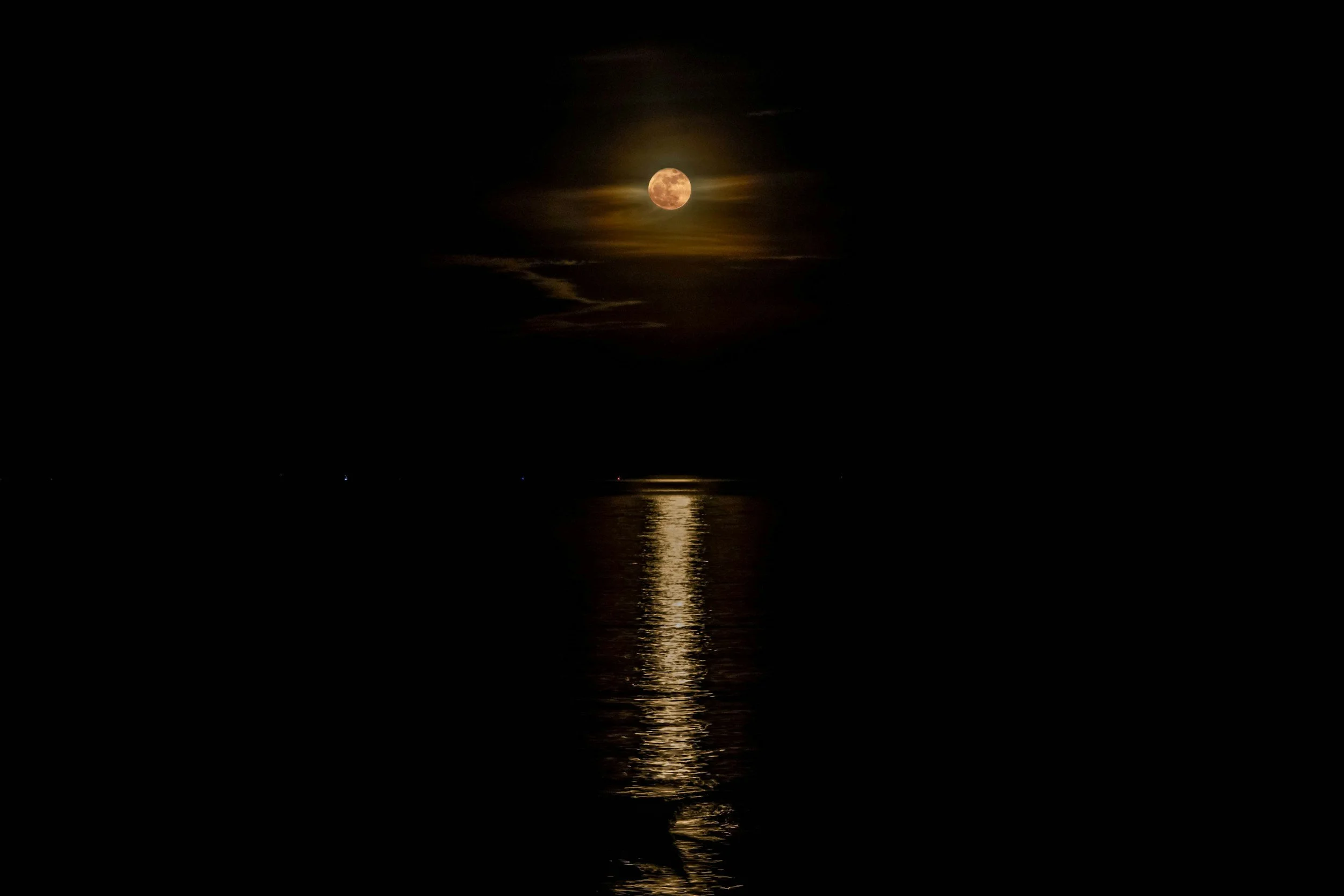 Full moon in a night sky with some clouds, reflected on a body of water.