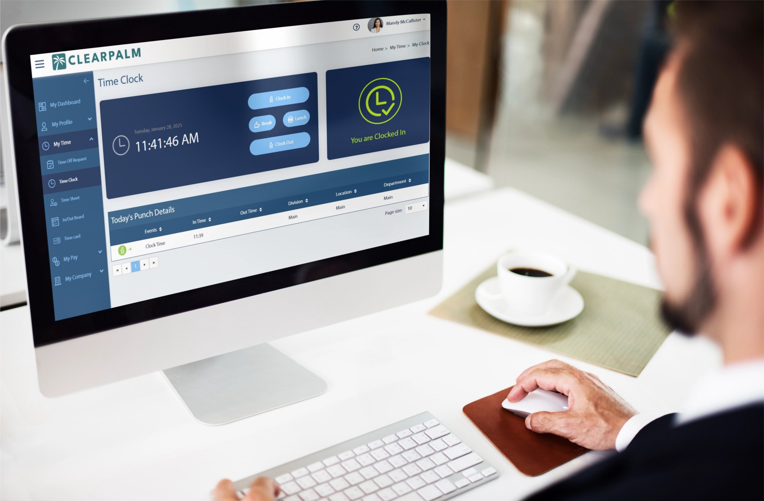 A person using a desktop computer with a time tracking software on the screen, showing clock-in and clock-out options, current time, and punch details in a workspace with a cup of coffee nearby.