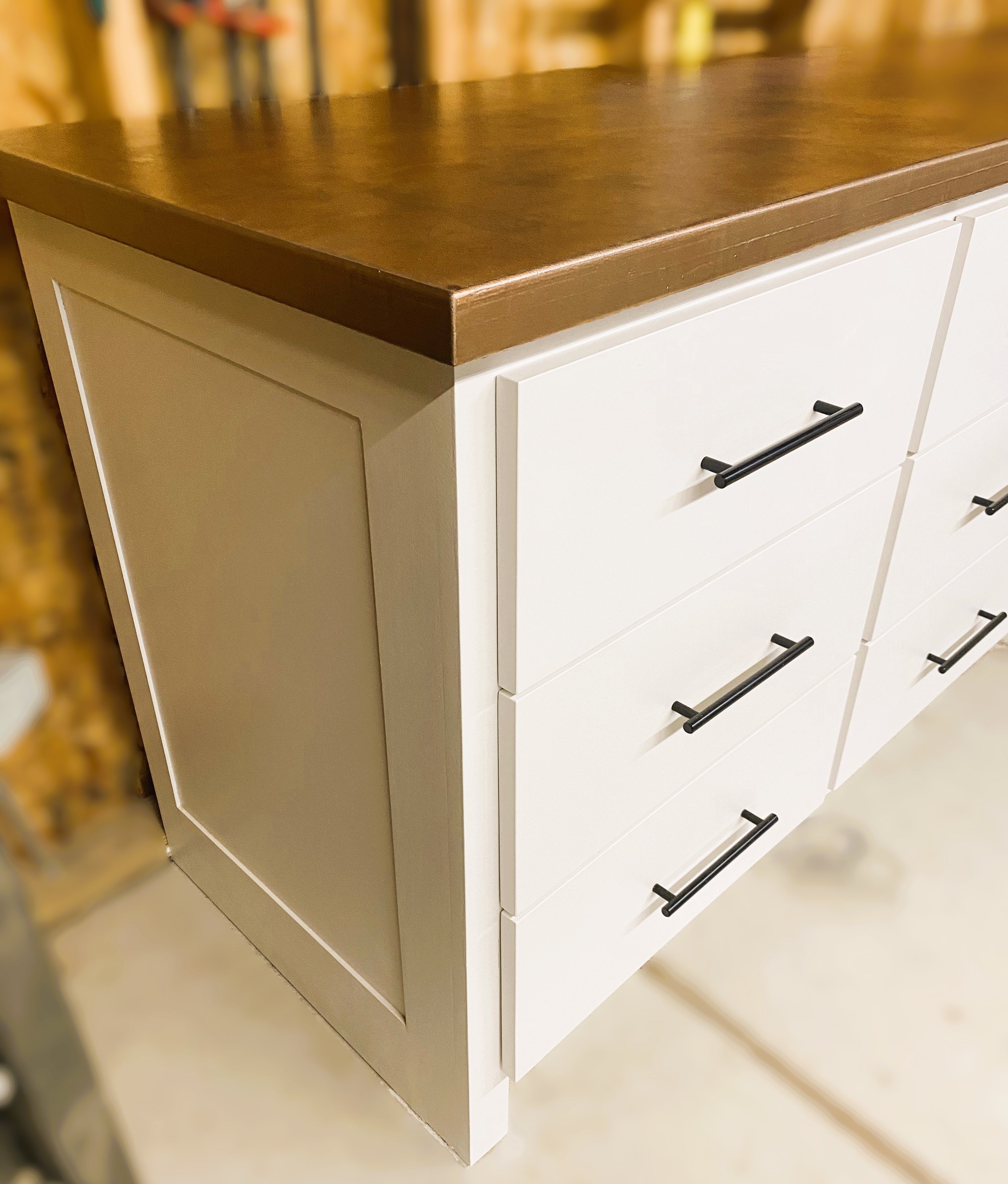 Close-up of a modern white dresser with black handles and a dark wood top.
