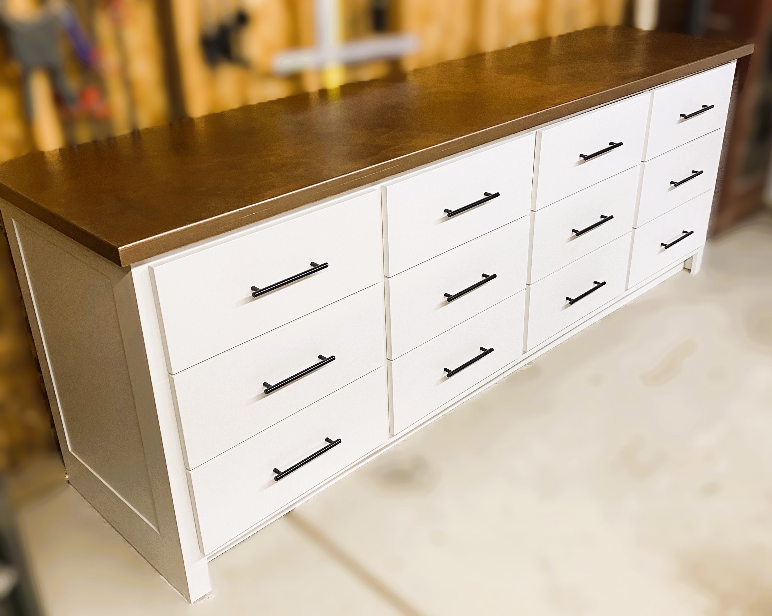 White modern sideboard with multiple drawers and black handles, topped with a dark wood surface.