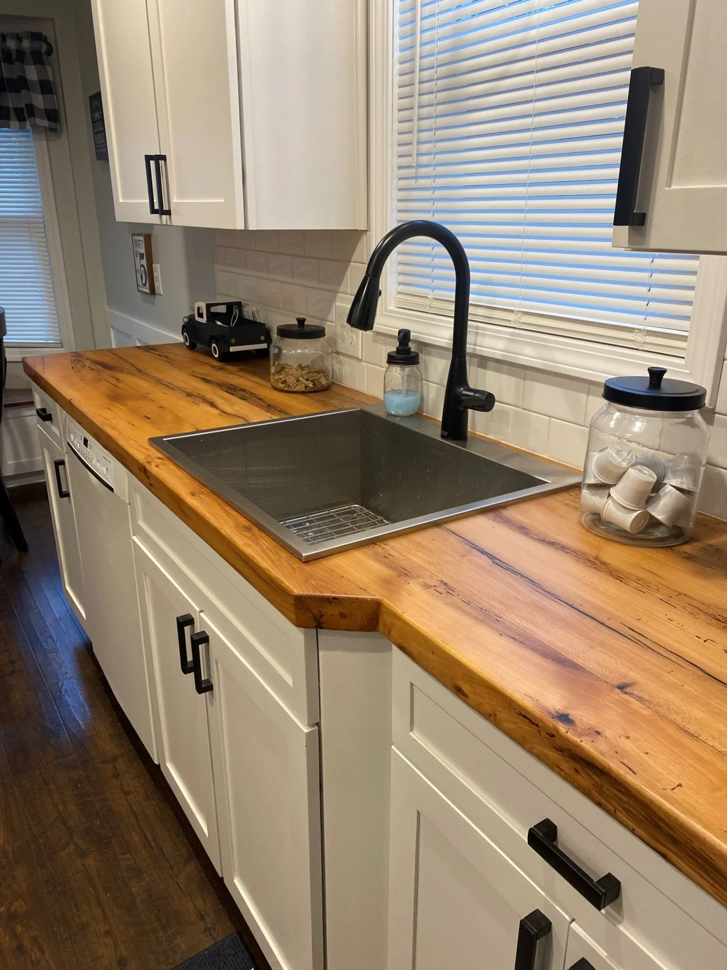 Kitchen counter with white cabinets, a black sink, black faucet, wooden countertop, and various jars and containers.