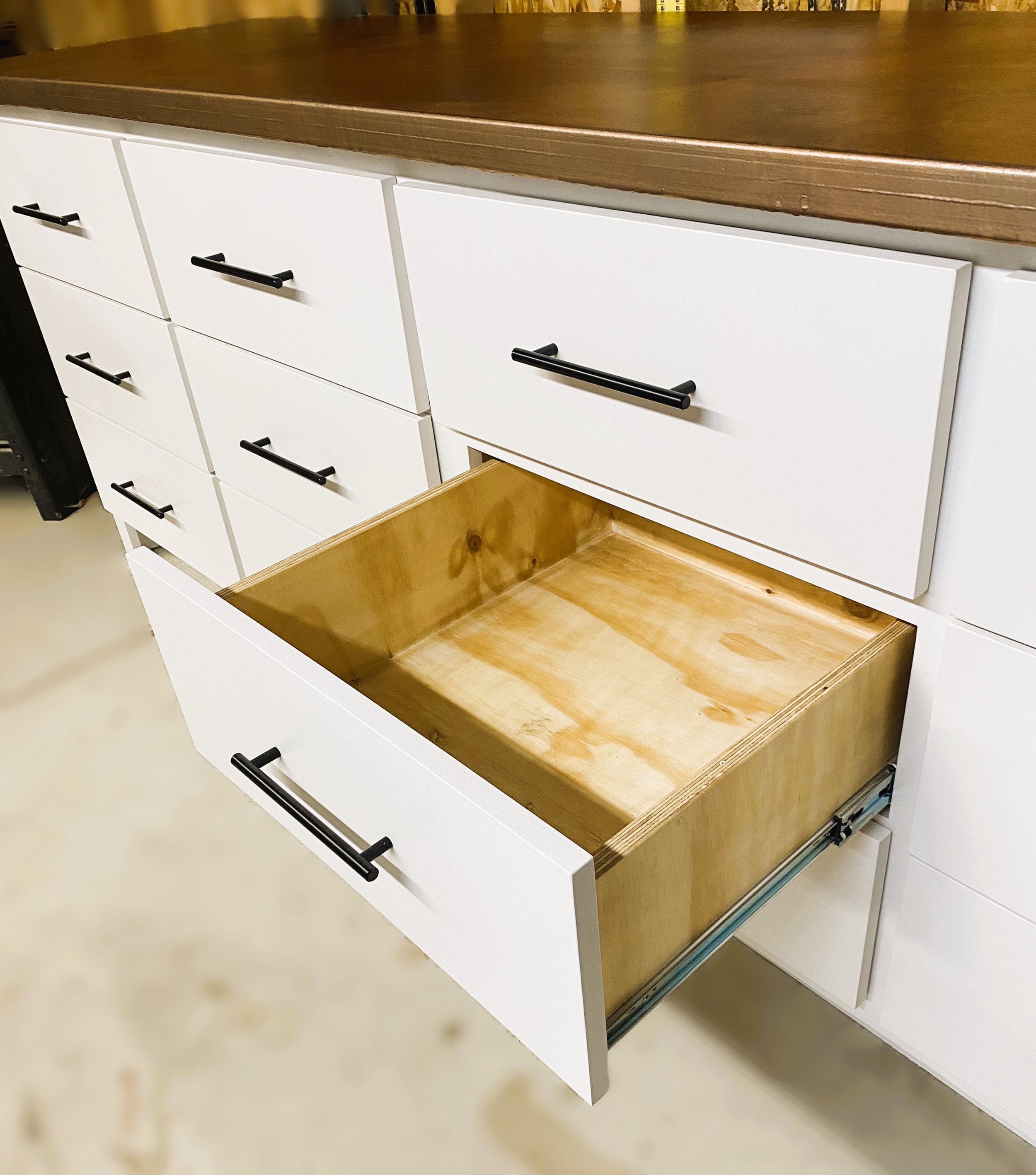 Open drawer of a white kitchen cabinet with black handles, revealing an empty wooden interior.