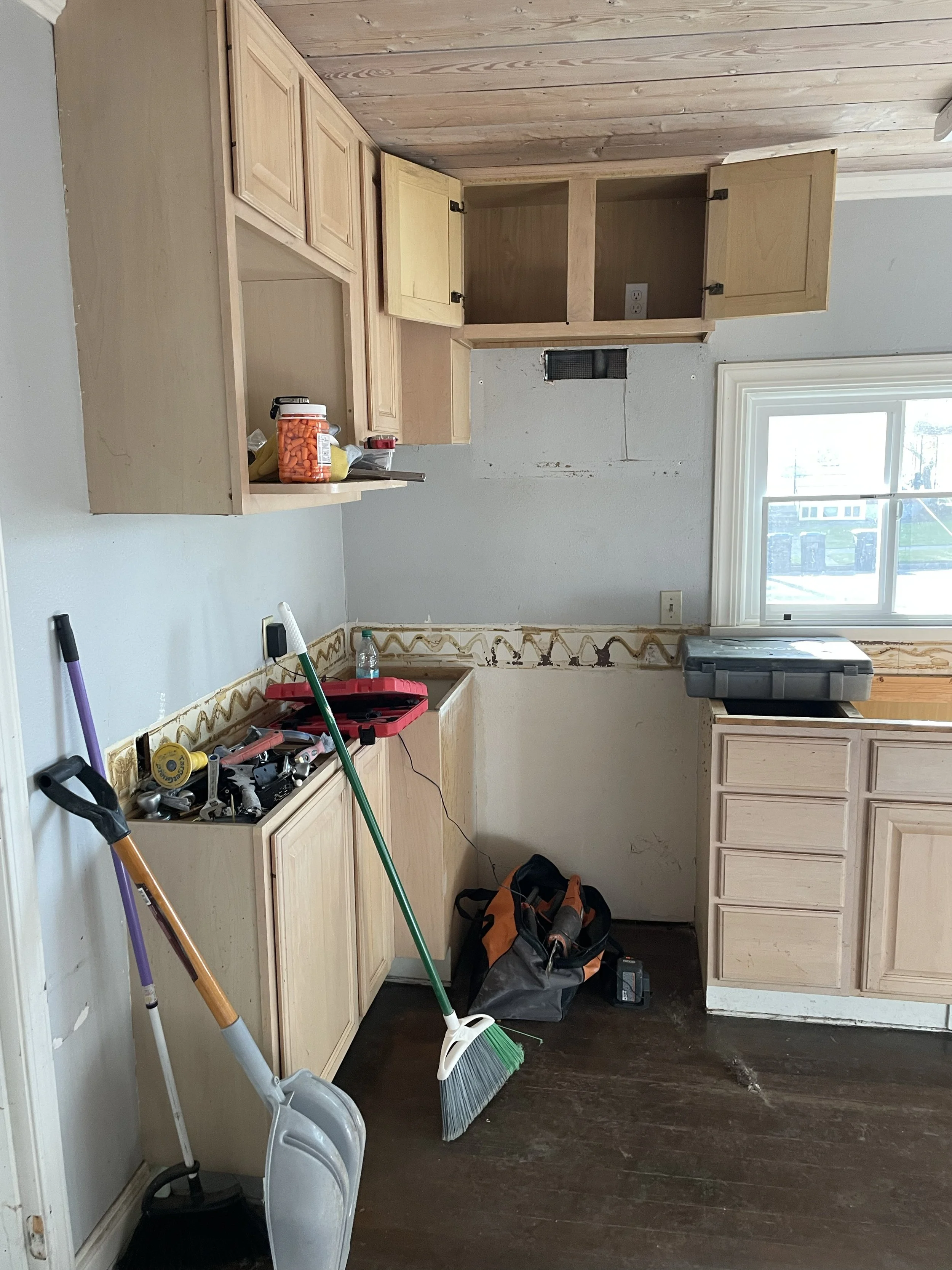 Kitchen under renovation with unfinished cabinets, tools, cleaning supplies, and a window providing natural light.