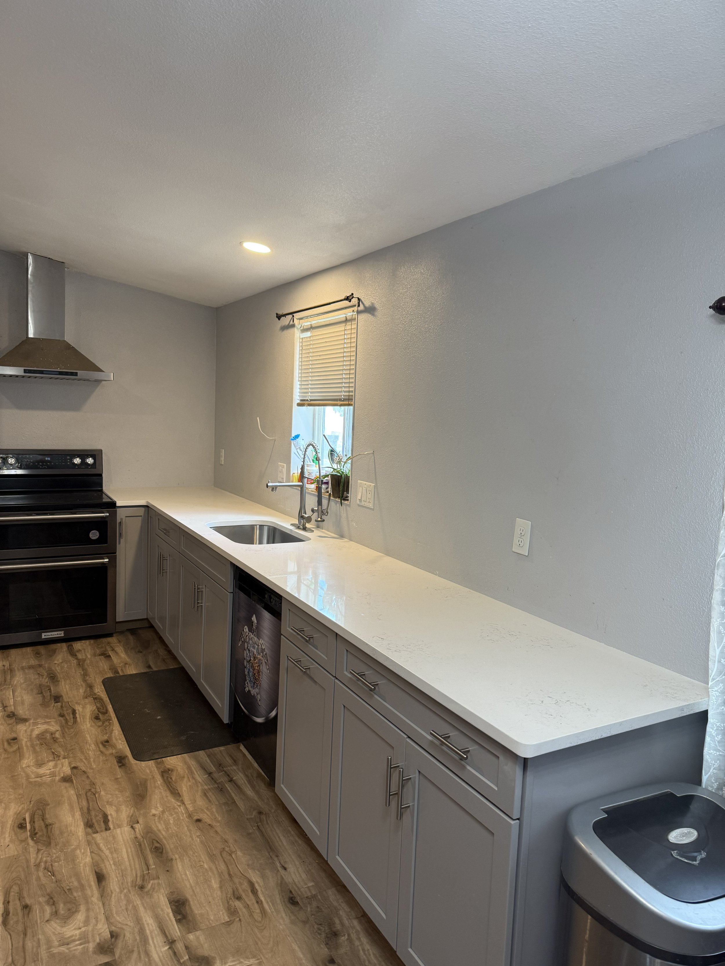 Modern kitchen with gray cabinets, white marble countertop, stainless steel appliances, and wood flooring.