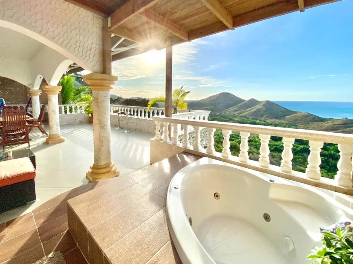 Terrasse avec vue sur montagnes et océan, baignoire, mobilier en bois.