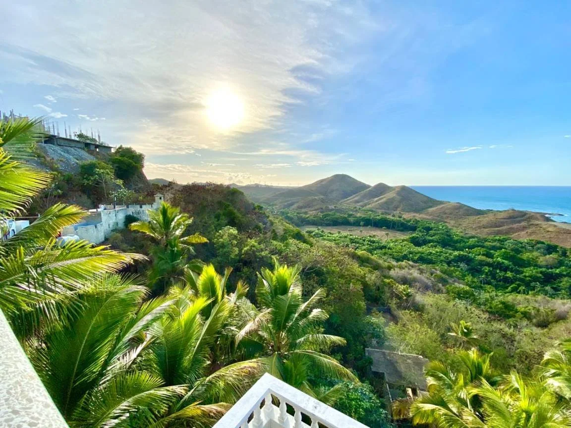 Paysage de plage avec coucher de soleil, collines verdoyantes et palmiers.
