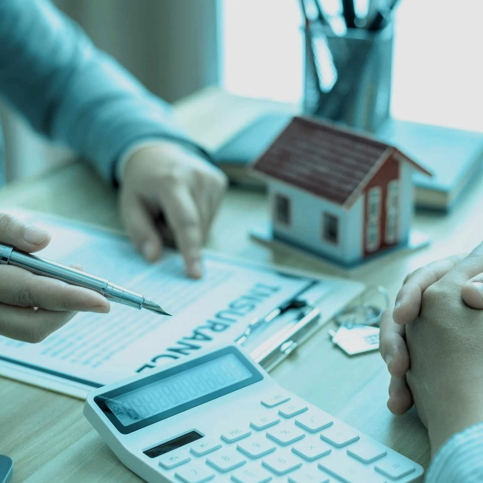 Personnes discutant d'un document d'assurance avec une calculatrice et une maquette de maison sur la table.