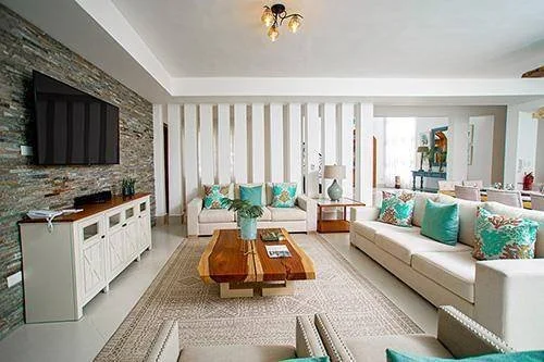 Salon moderne avec canapé beige, coussins turquoise et multicolores, tables basses en bois, télévision murale, décoration intérieure lumineuse.