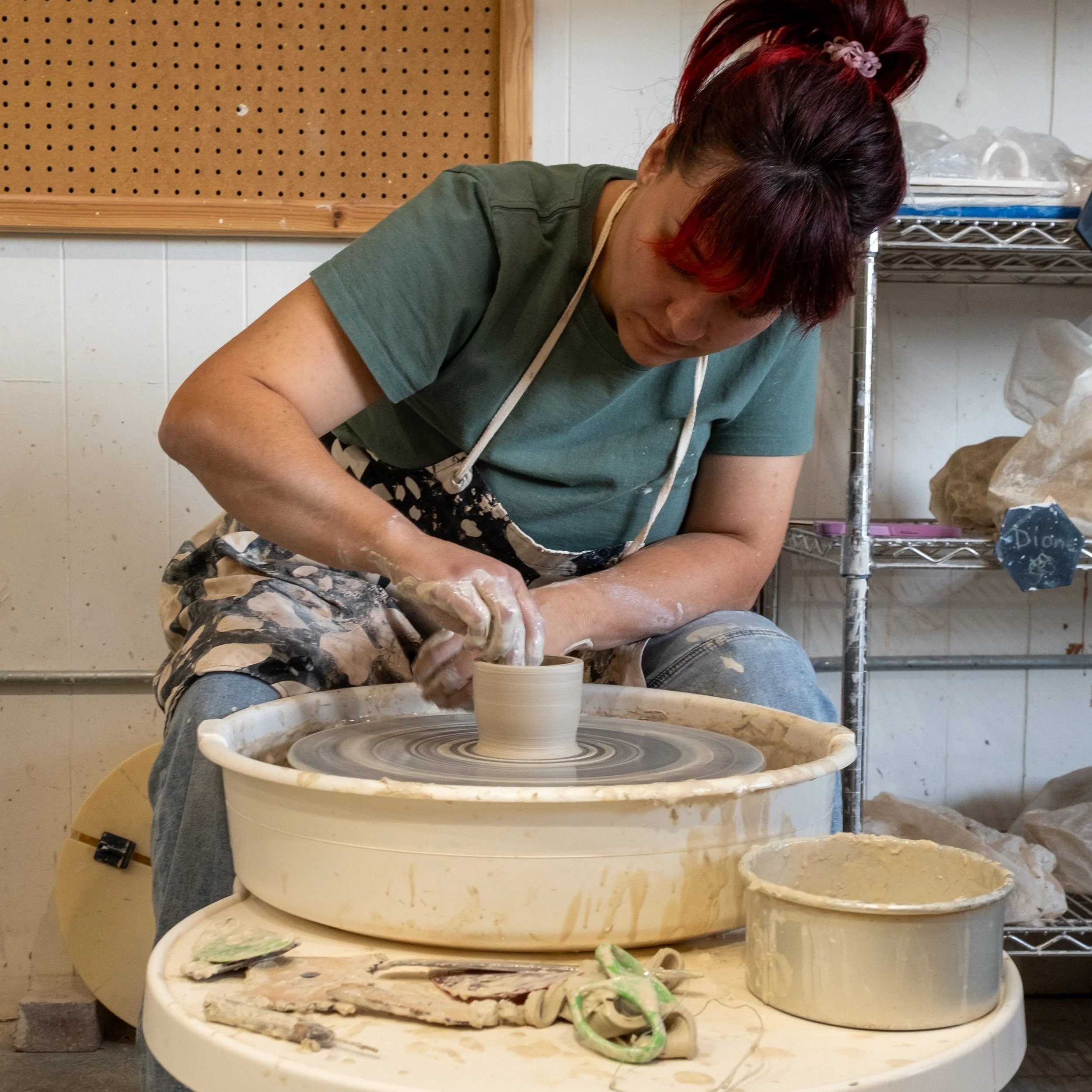 Person shaping clay on a pottery wheel in a ceramics studio.