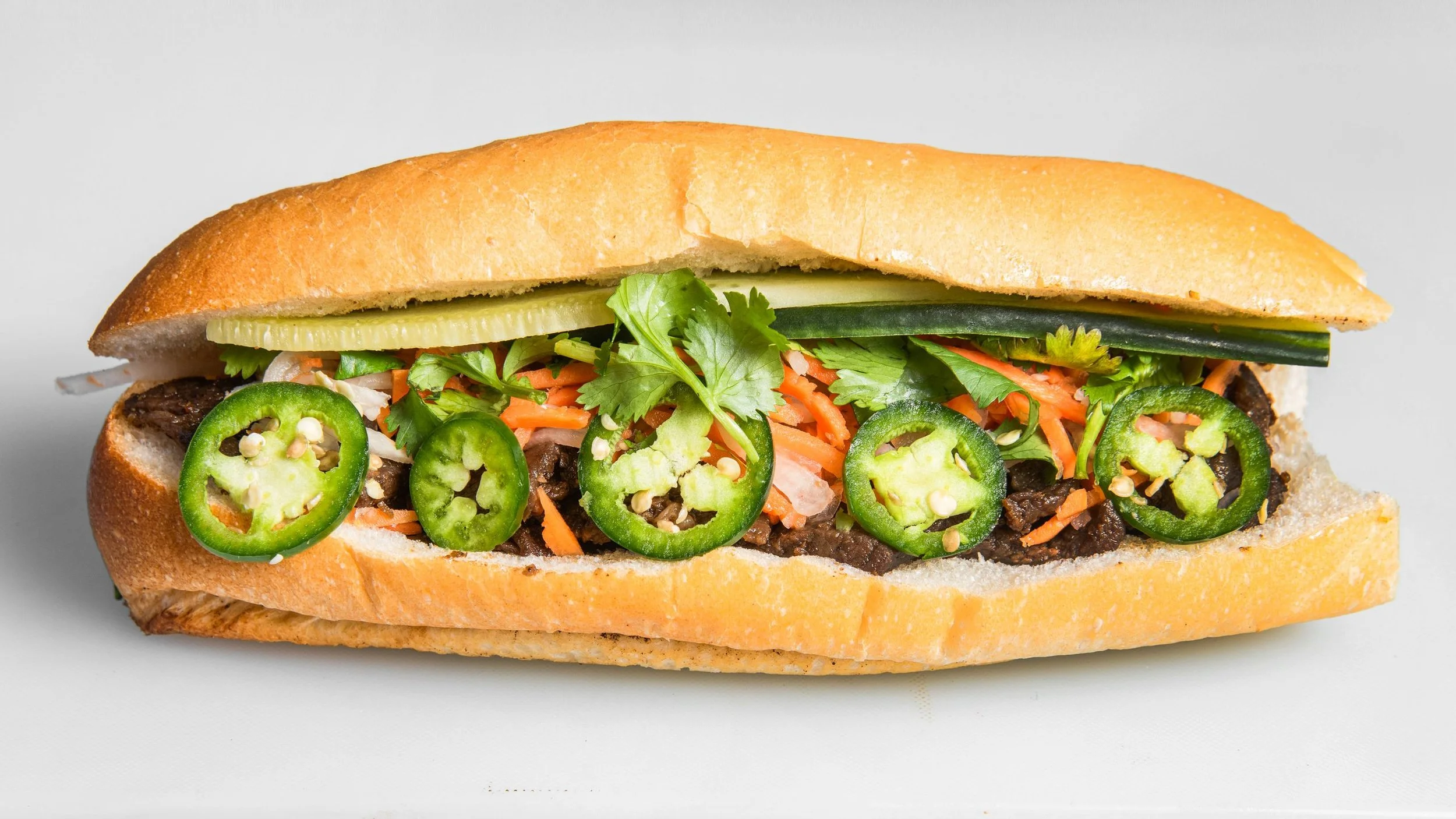 Crispy Fresh Toasted Vietnamese Sandwich Banh Mi with traditional vietnamese cold cuts including vietnamese ham with cucumber, cilantro, jalapeño, pickled carrot daikon, pate, garlic spread