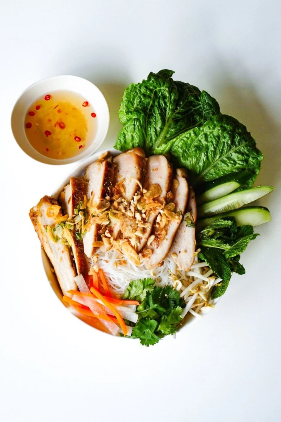 Noodle bowl top with fresh veggies, protein, and a side of fish sauce