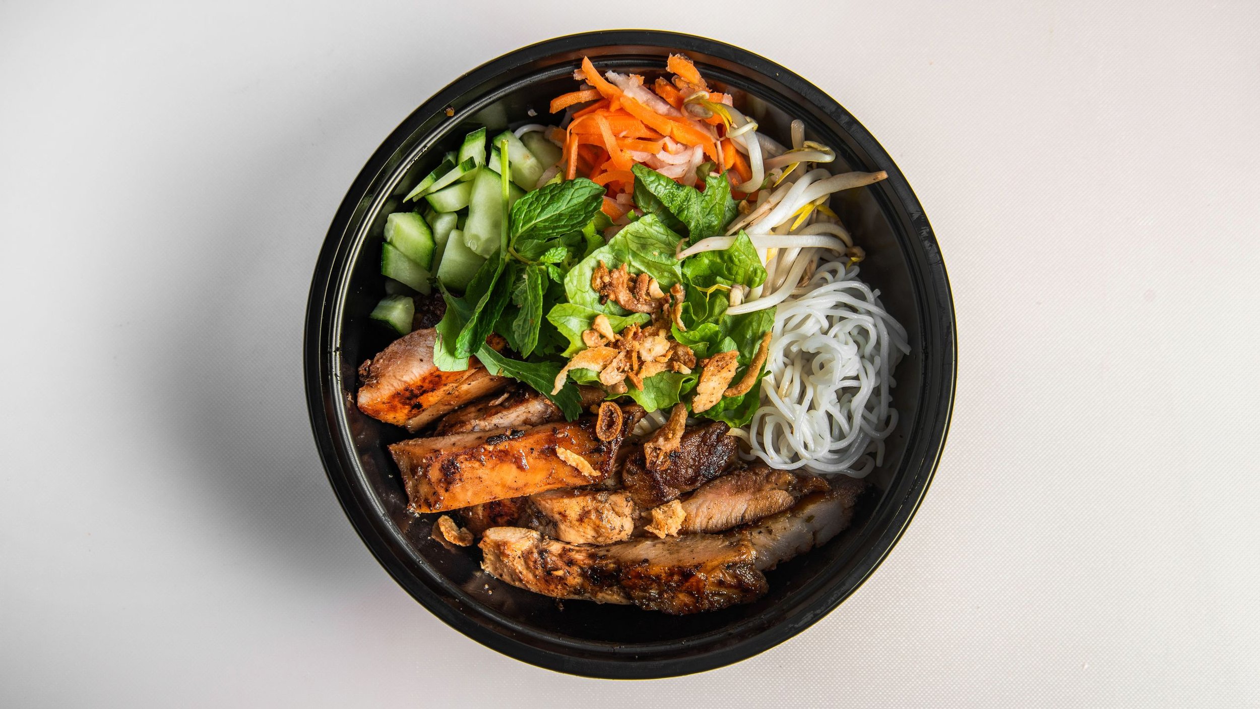 Bowl of vietnamese vermicelli noodles topped with grilled chicken, grilled pork, grilled beef, or fried tofu with fresh veggies, roasted peanuts, green onion oil, and side of citrus fish sauce