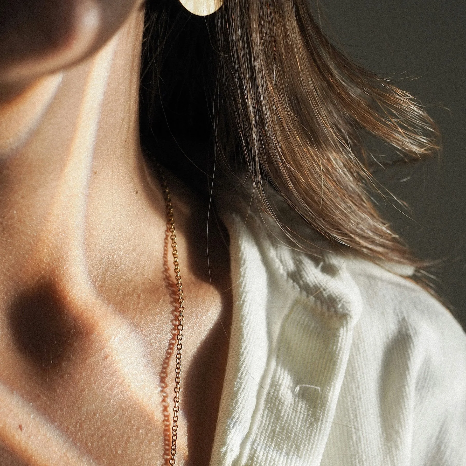 Close-up of a woman's neck wearing a gold chain necklace with a white shirt.