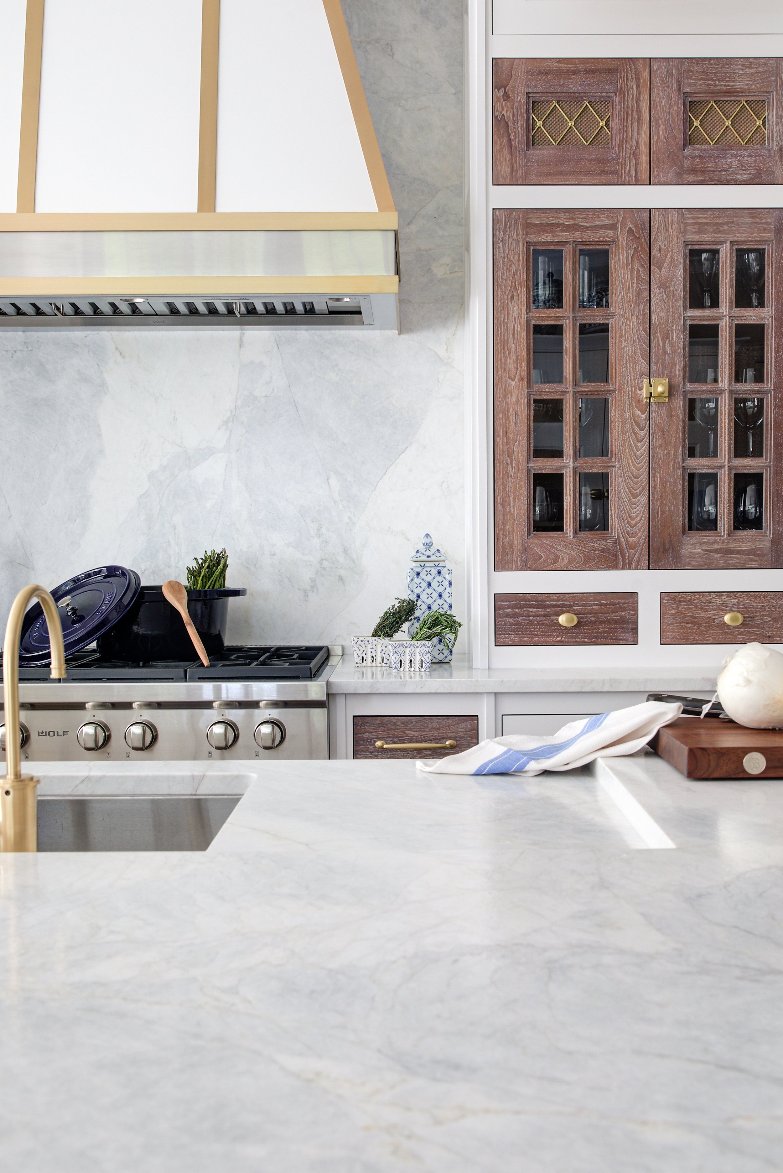 High-end kitchen and interior design in Fairfield County CT & Charlotte, NC: custom brass-trim hood with marble slab backsplash and warm wood cabinetry, New Canaan CT.