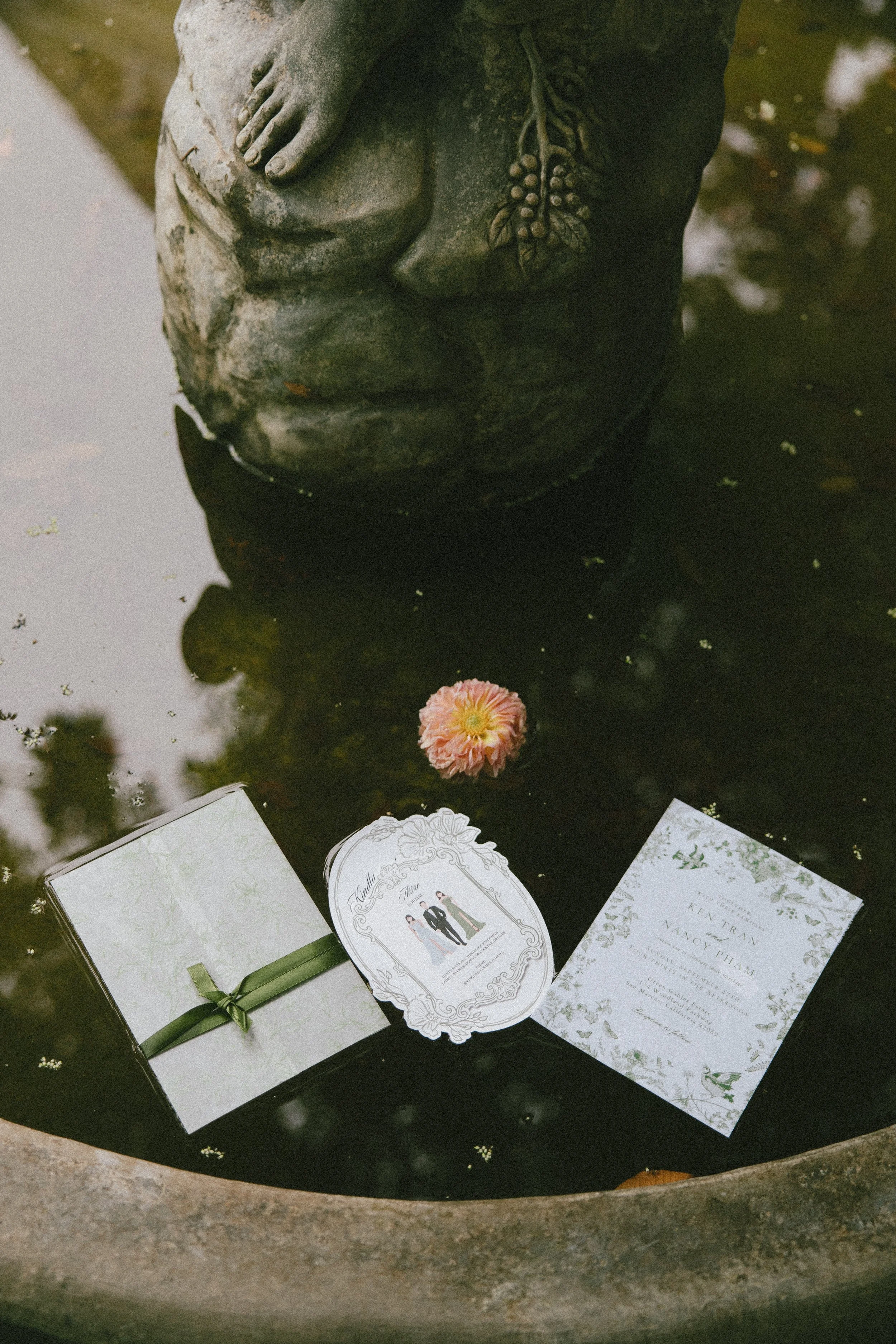 Wedding invitations and a pink bloom floating on a stone fountain at Green Gables Wedding Estate