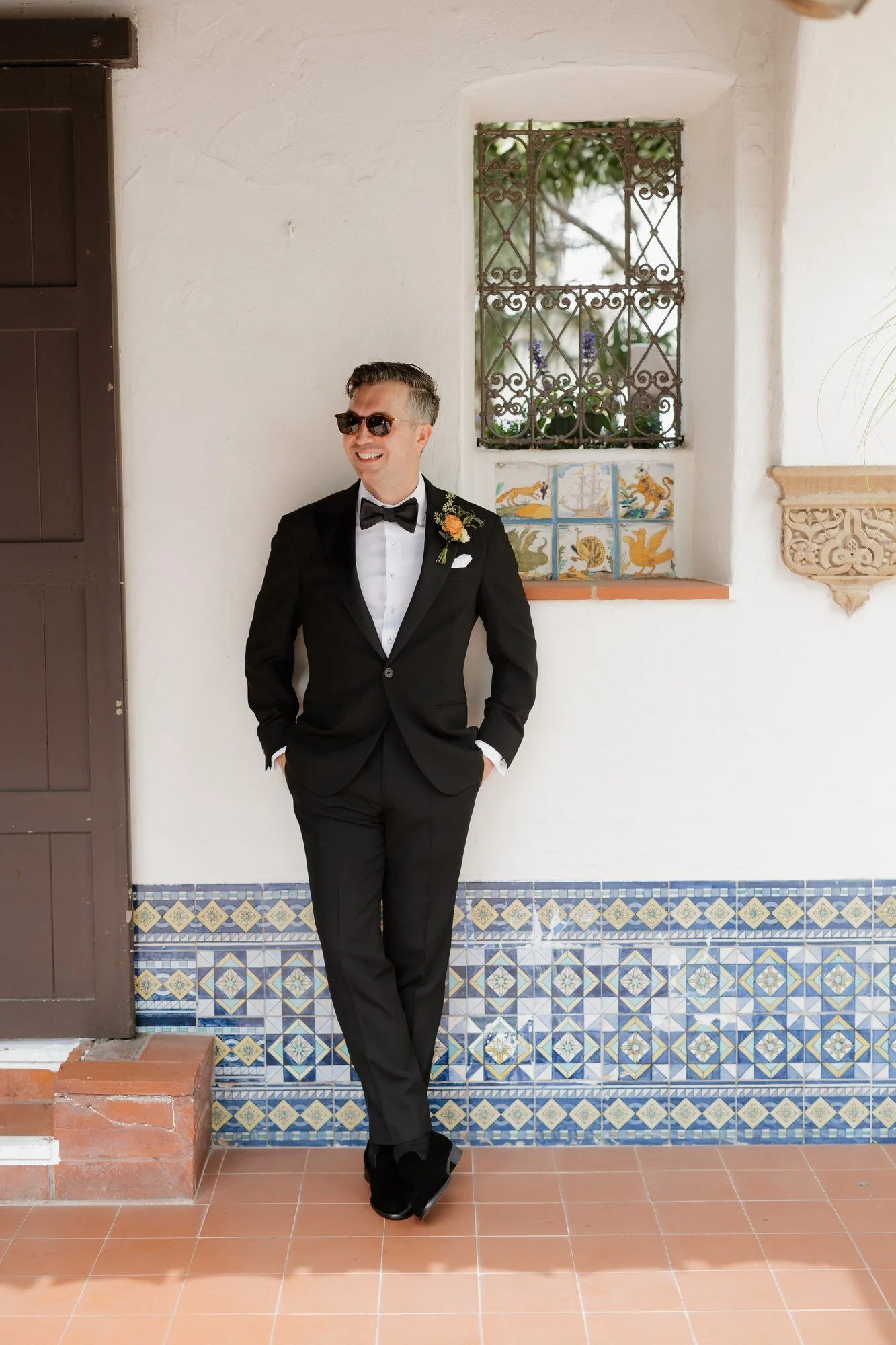 Groom in black tuxedo leaning against Spanish tile at Darlington House