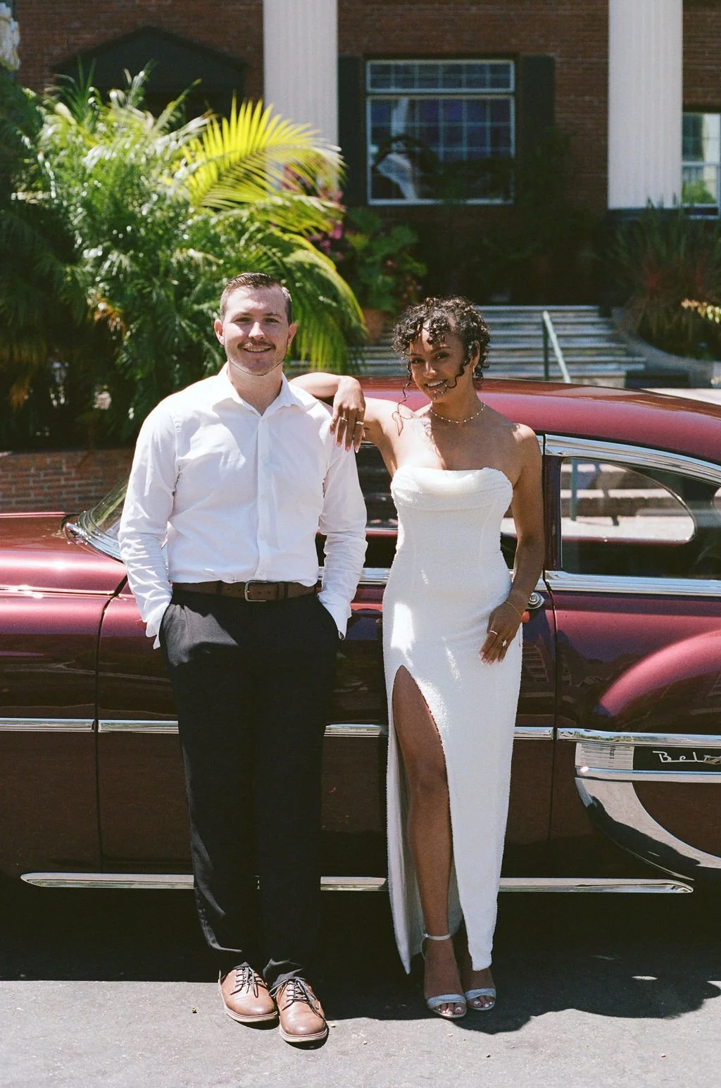 Couple posing with a vintage car in front of the Lafayette Hotel's colonial facade in North Park
