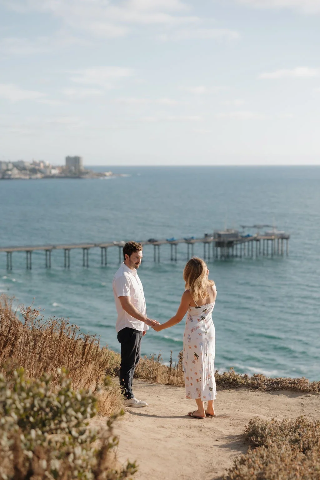 Couple holding hands on the bluff with Scripps Pier behind them