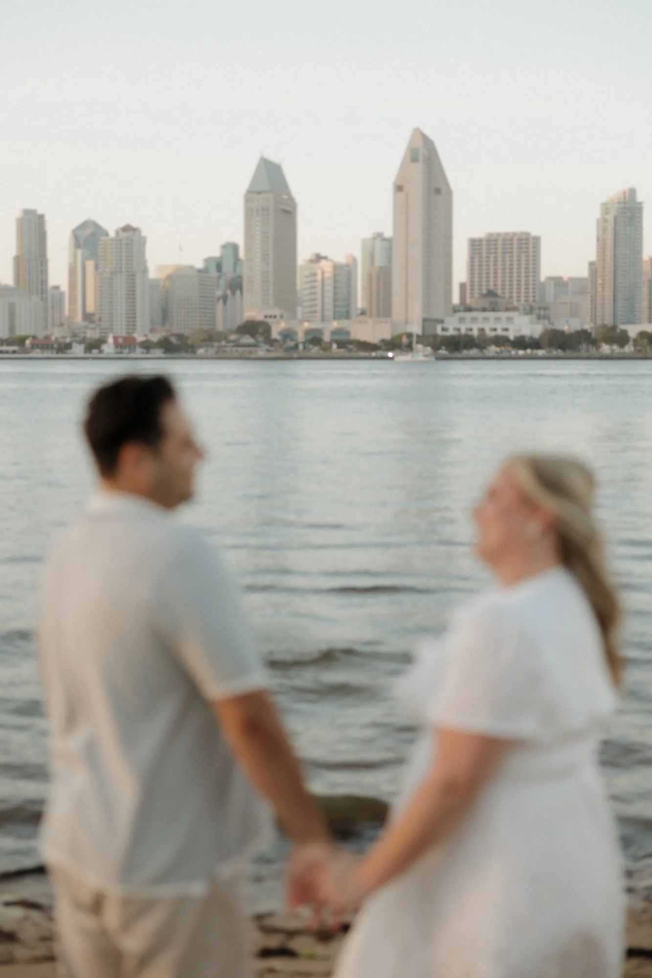 Couple holding hands in front of the San Diego skyline at Centennial Park, Coronado