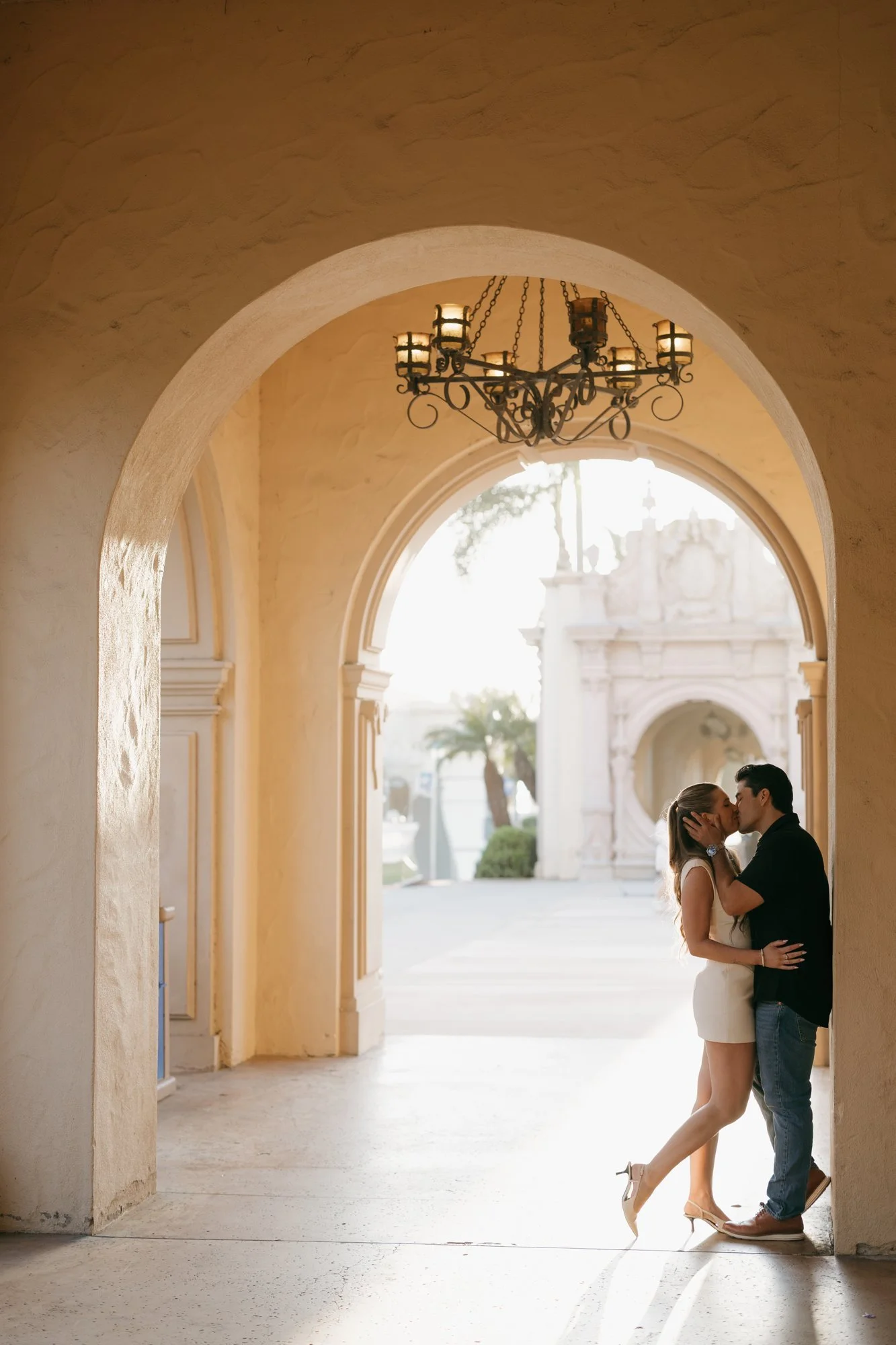 Couple kissing beneath a wrought-iron chandelier in a Balboa Park arcade